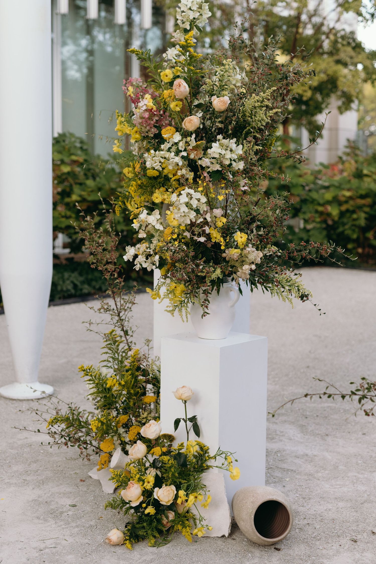 Elegant floral arrangement with yellow and white flowers on white pedestal.