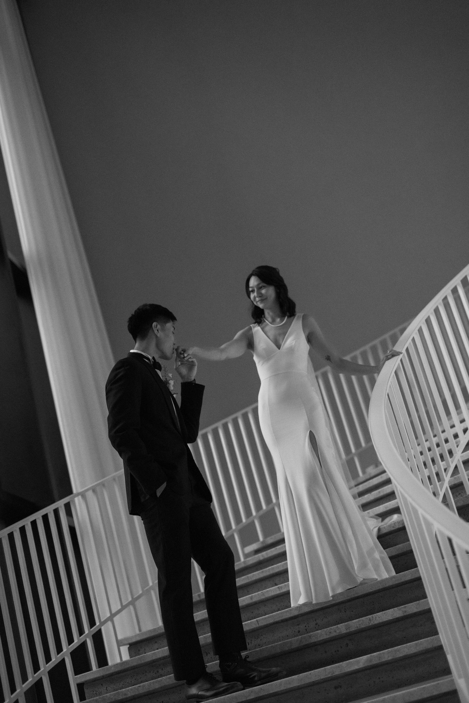 A romantic moment captured on an elegant white staircase in black and white photography.
