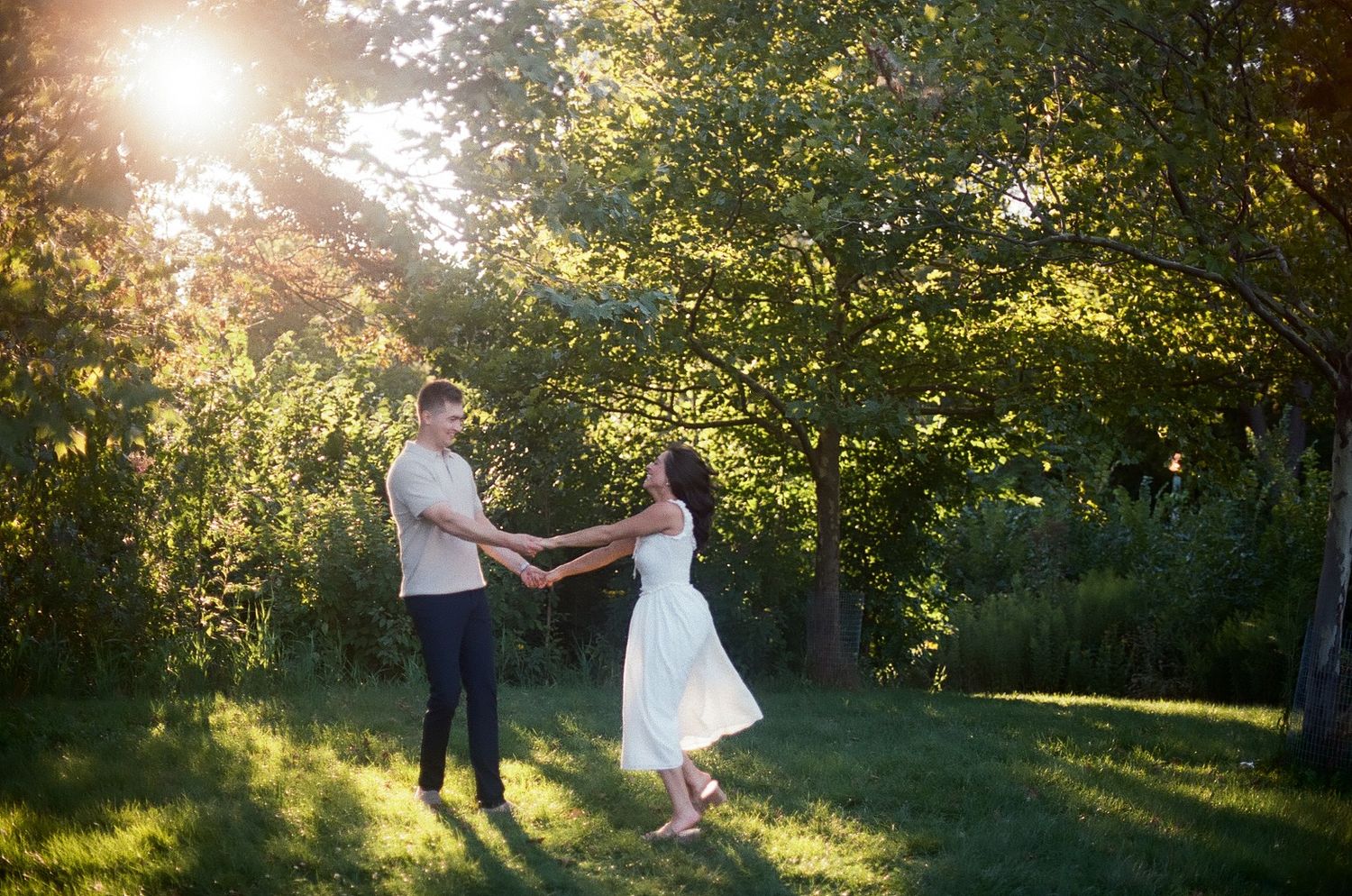 Golden sunlight streams through trees as newlyweds twirl and dance in a lush garden setting.