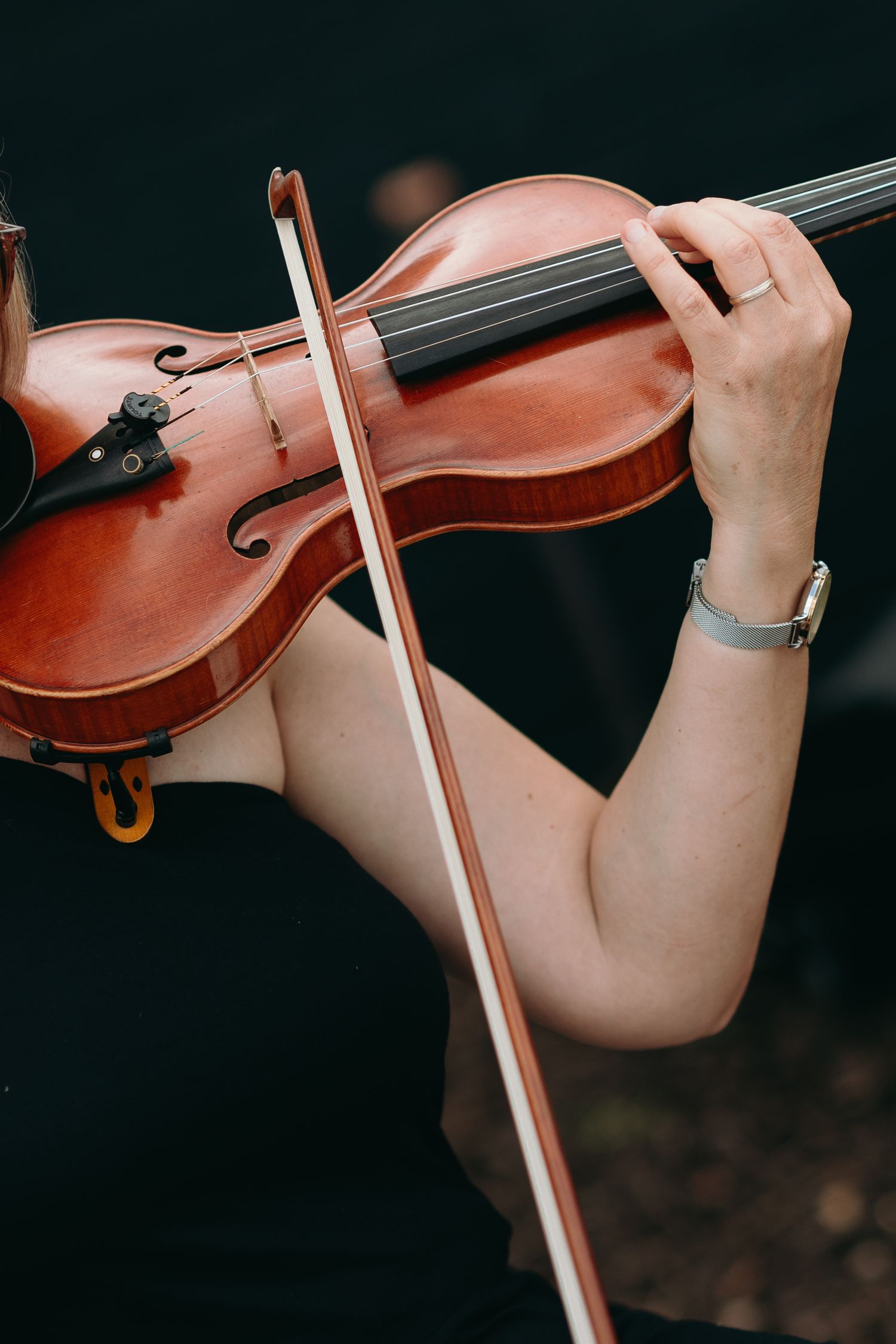 Close-up shot of hands playing a wooden violin with bow against dark background.