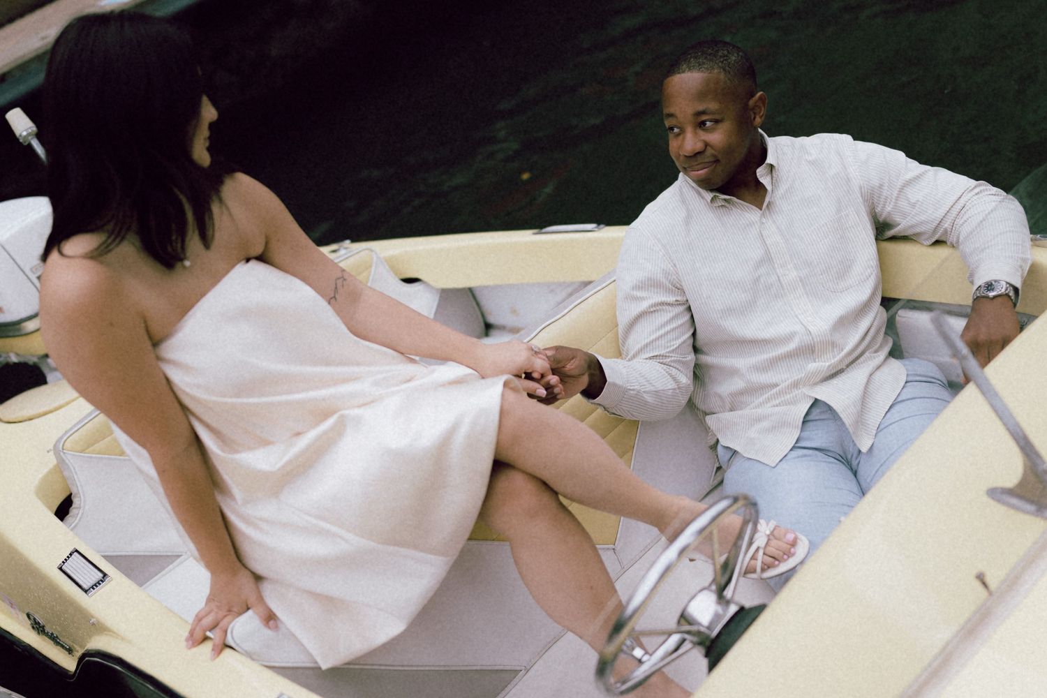 Couple holding hands on a luxury boat, woman in white dress and man in light blue shirt enjoying a romantic outing.
