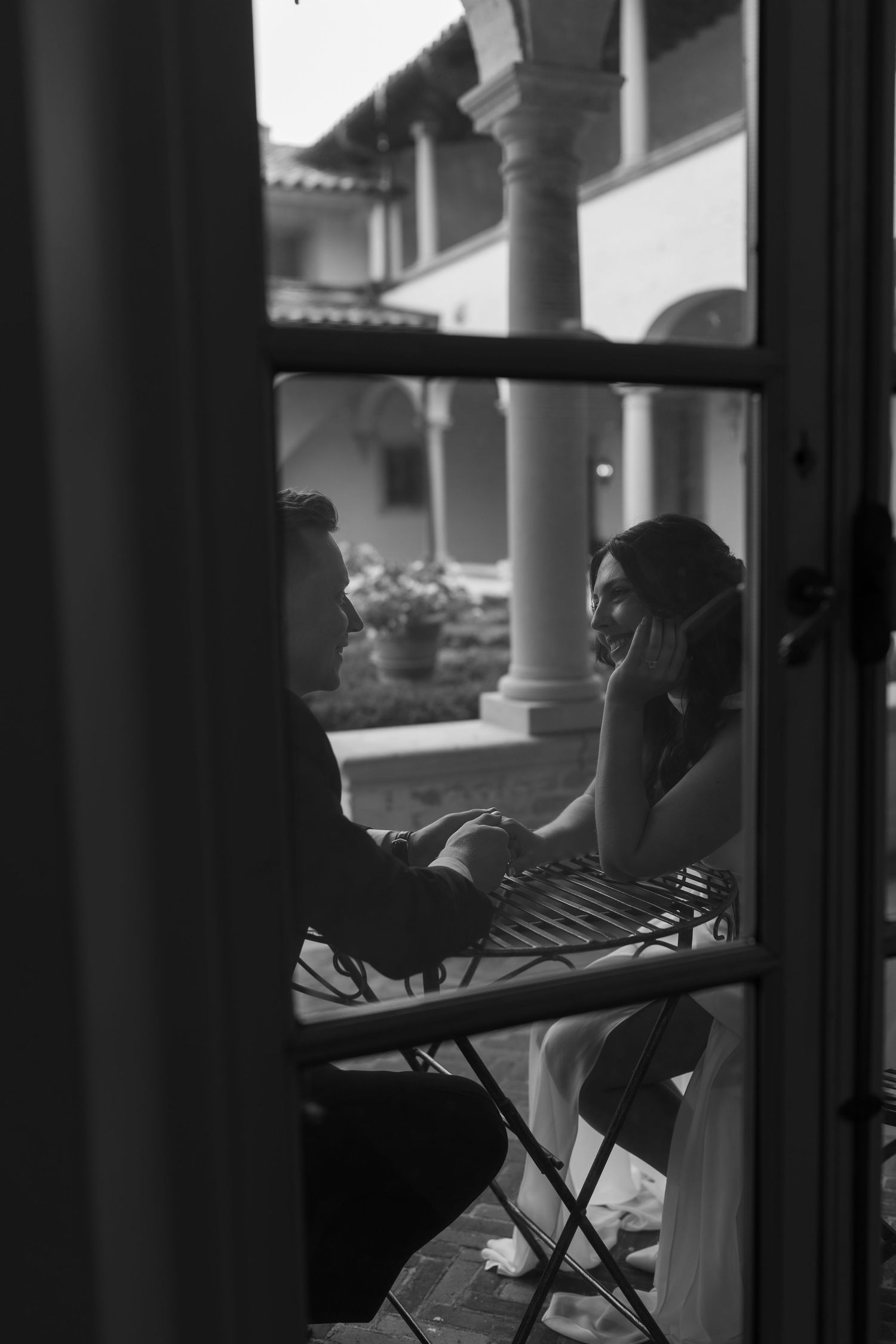 A black and white view through a window showing figures seated at an outdoor table beneath ornate columns. The Villa Terrace Milwaukee