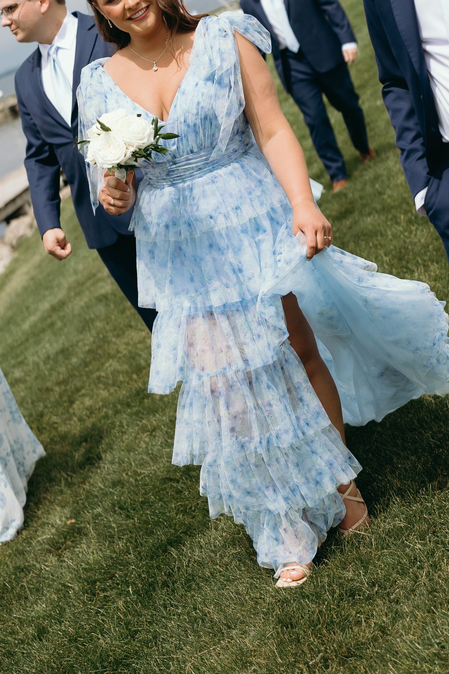 A person wearing a light blue floral dress twirls on green grass during an outdoor celebration.