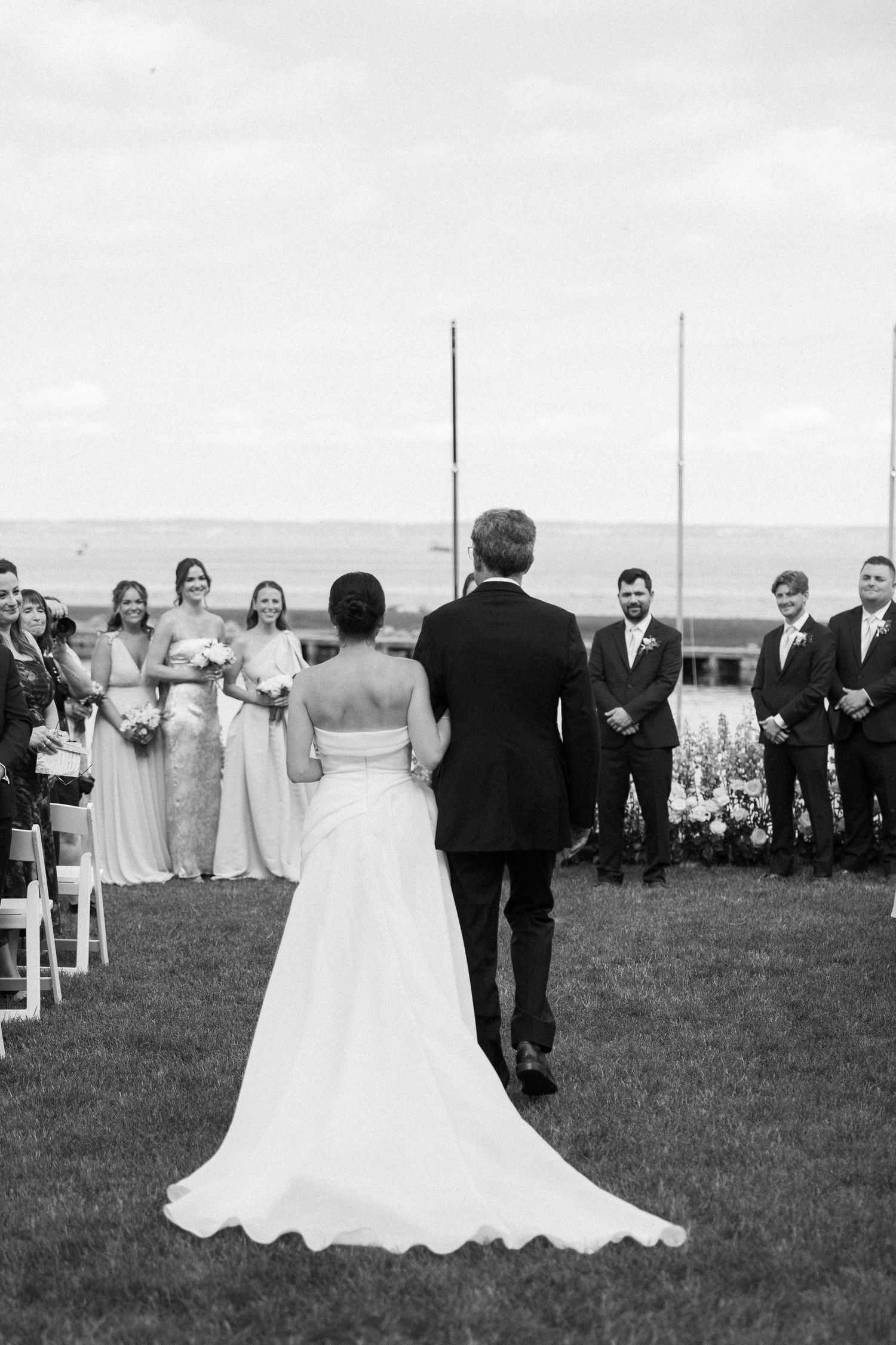 A black and white shot of a wedding ceremony on a hilltop lawn with the wedding party gathered outdoors.