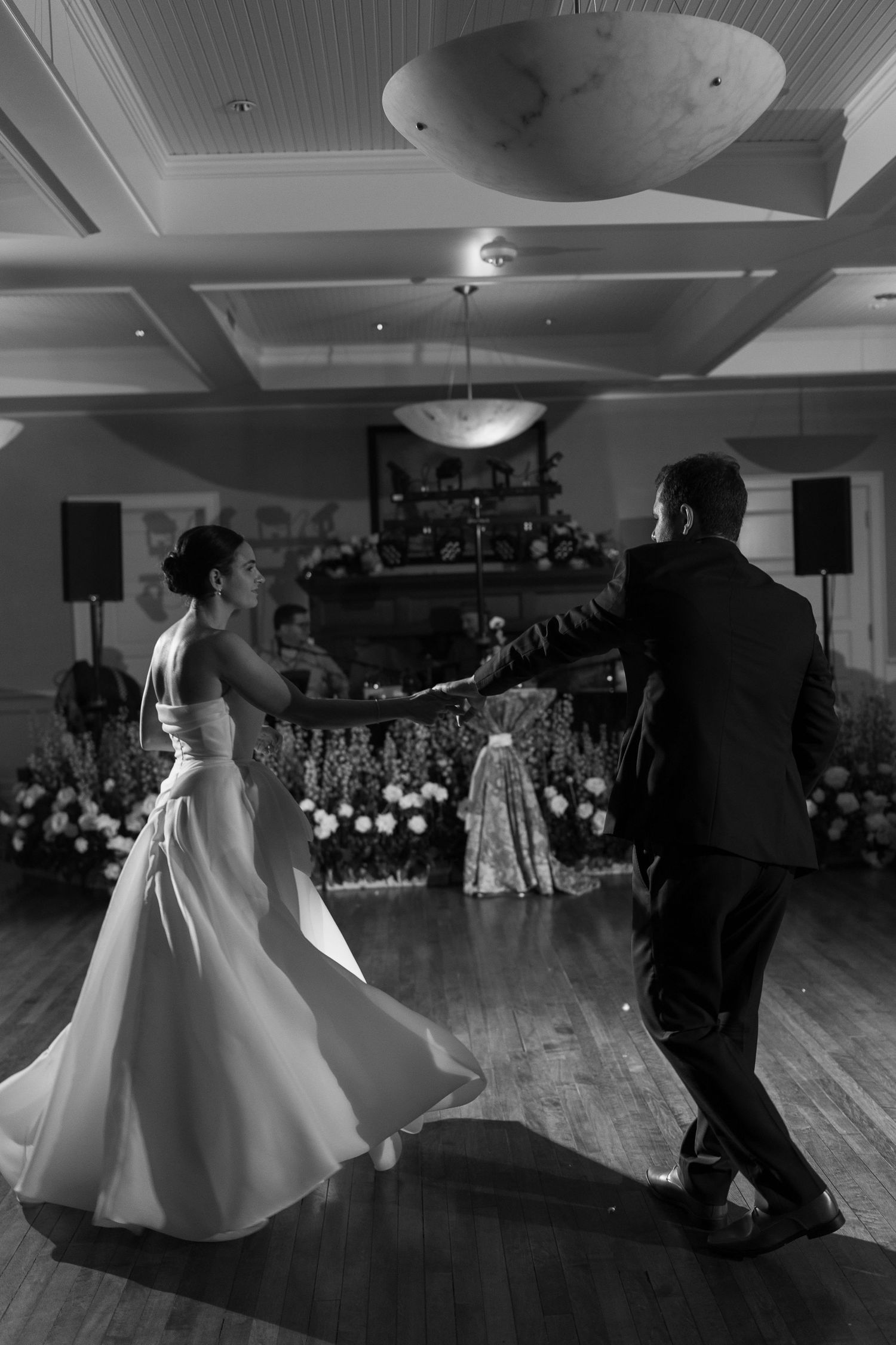 Dancing couples in formal attire glide across a spacious ballroom floor during an elegant dance event.