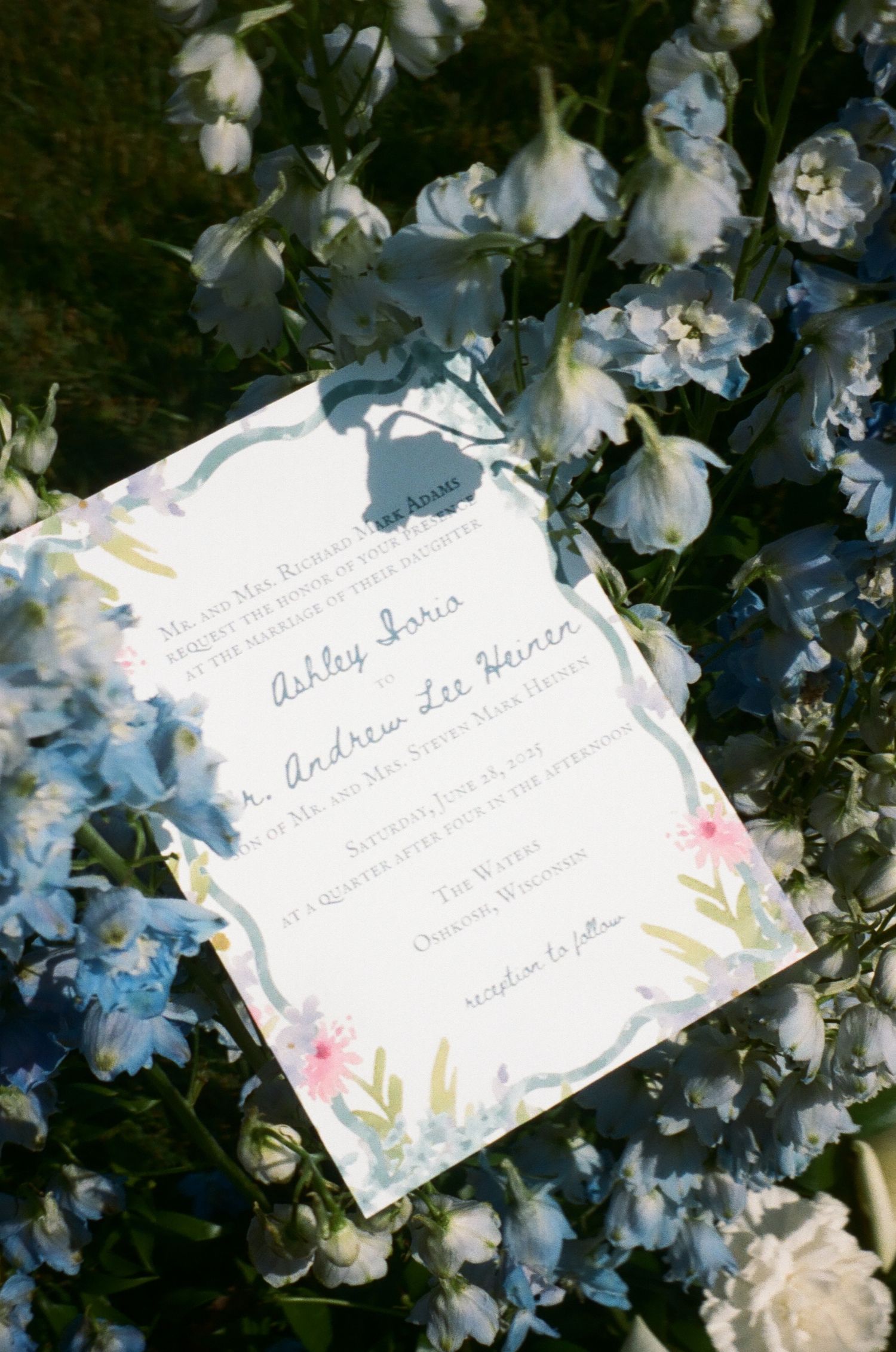 A white paper invitation card nestled among delicate white flowers with soft lighting and natural textures.