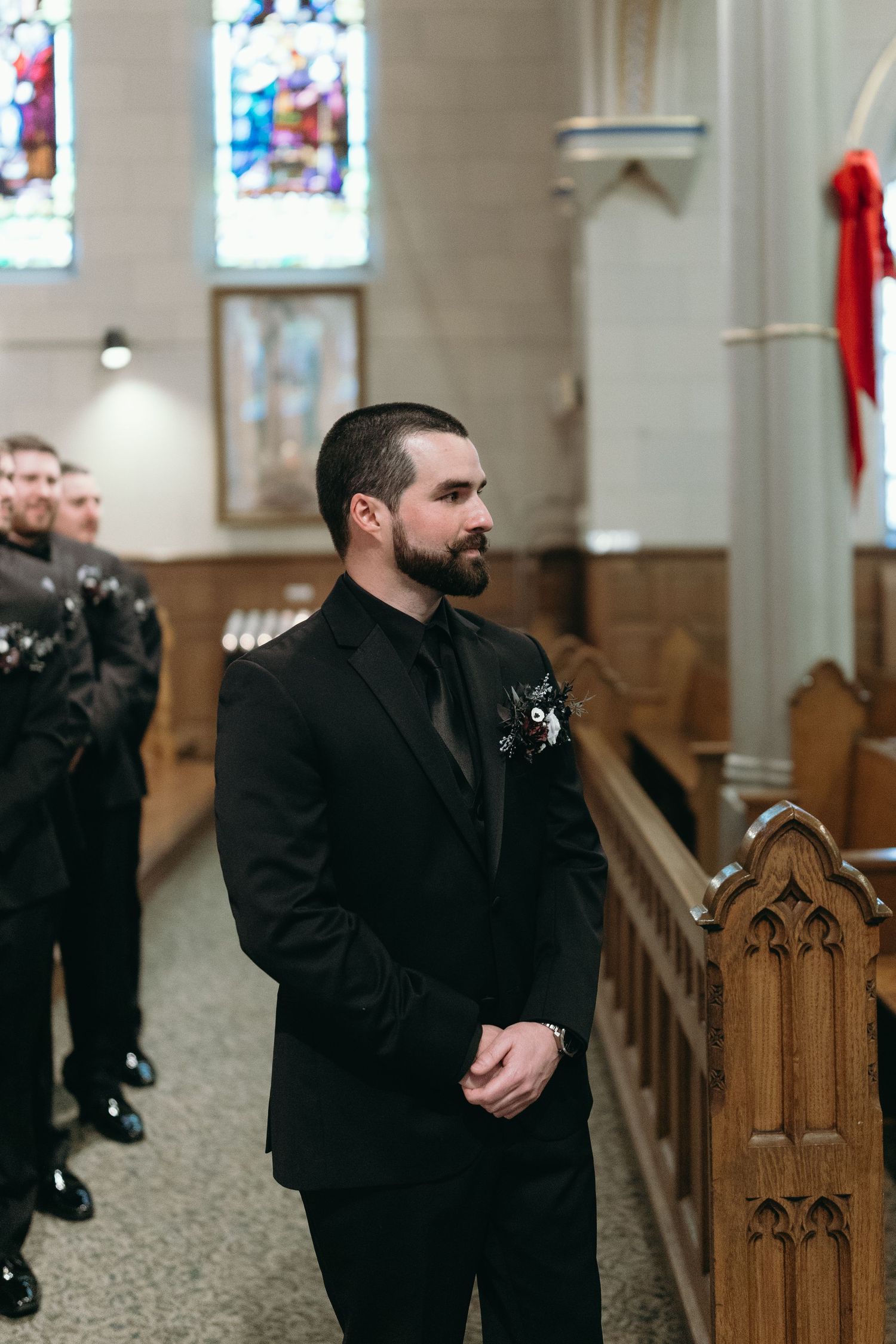 A solemn moment captured in a church as someone stands by ornate wooden pews during a wedding ceremony.