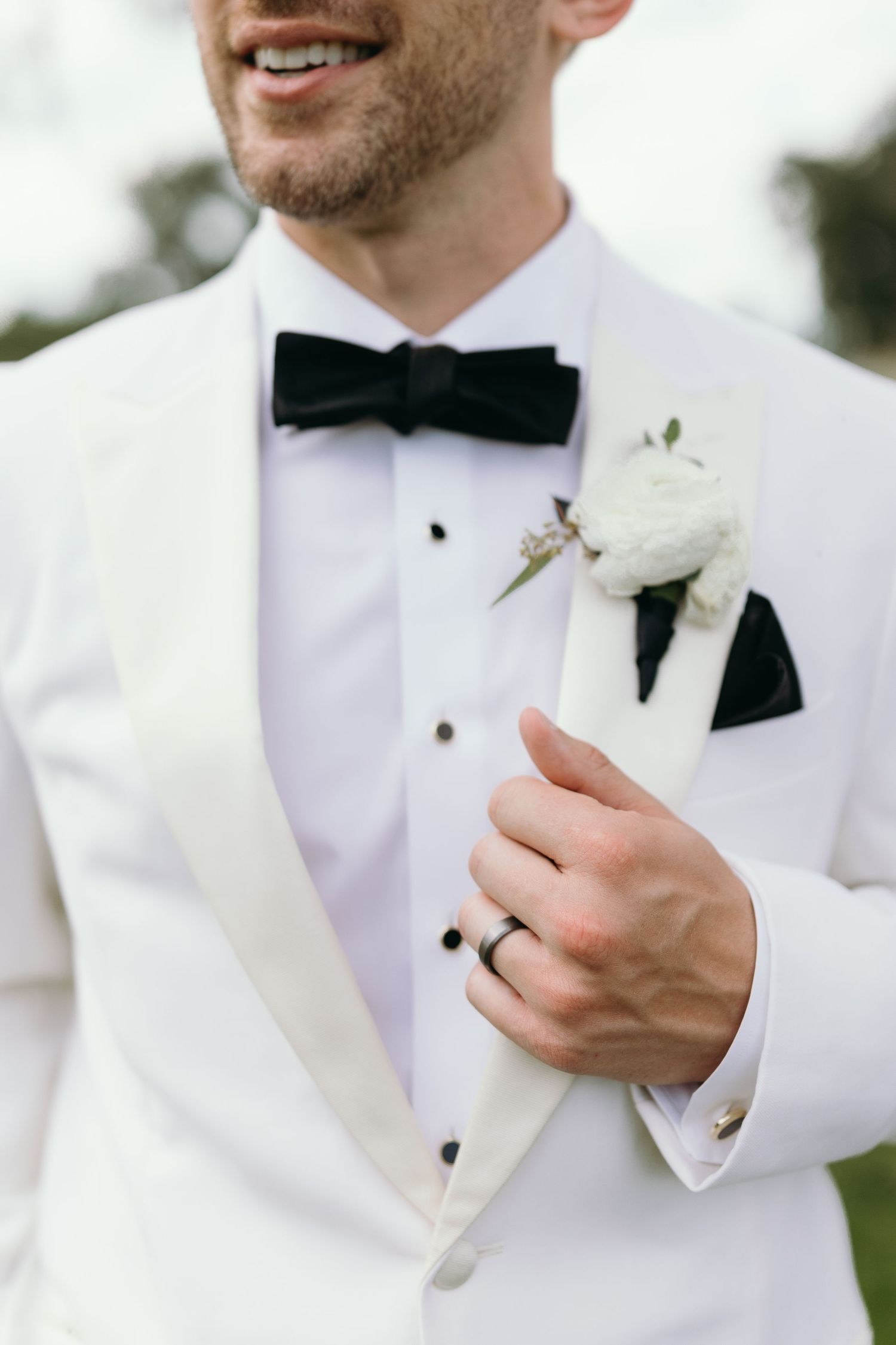 Detail shot of white tuxedo jacket with black bowtie and boutonniere.