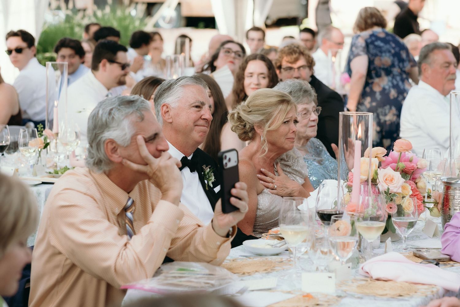 Guests seated at elegantly decorated wedding reception tables, enjoying the celebration under a white tent.