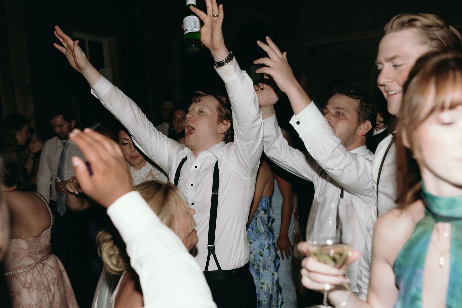 Guests dancing joyfully at a wedding reception, with a young boy in suspenders raising his arms in celebration.