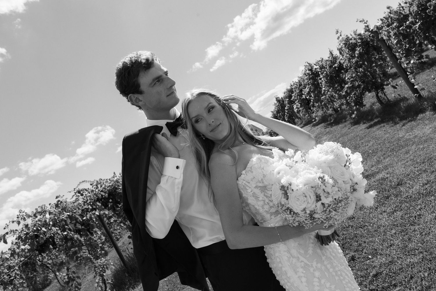 A black and white photo series shows a couple embracing and dancing together on a grassy hillside under clouds.