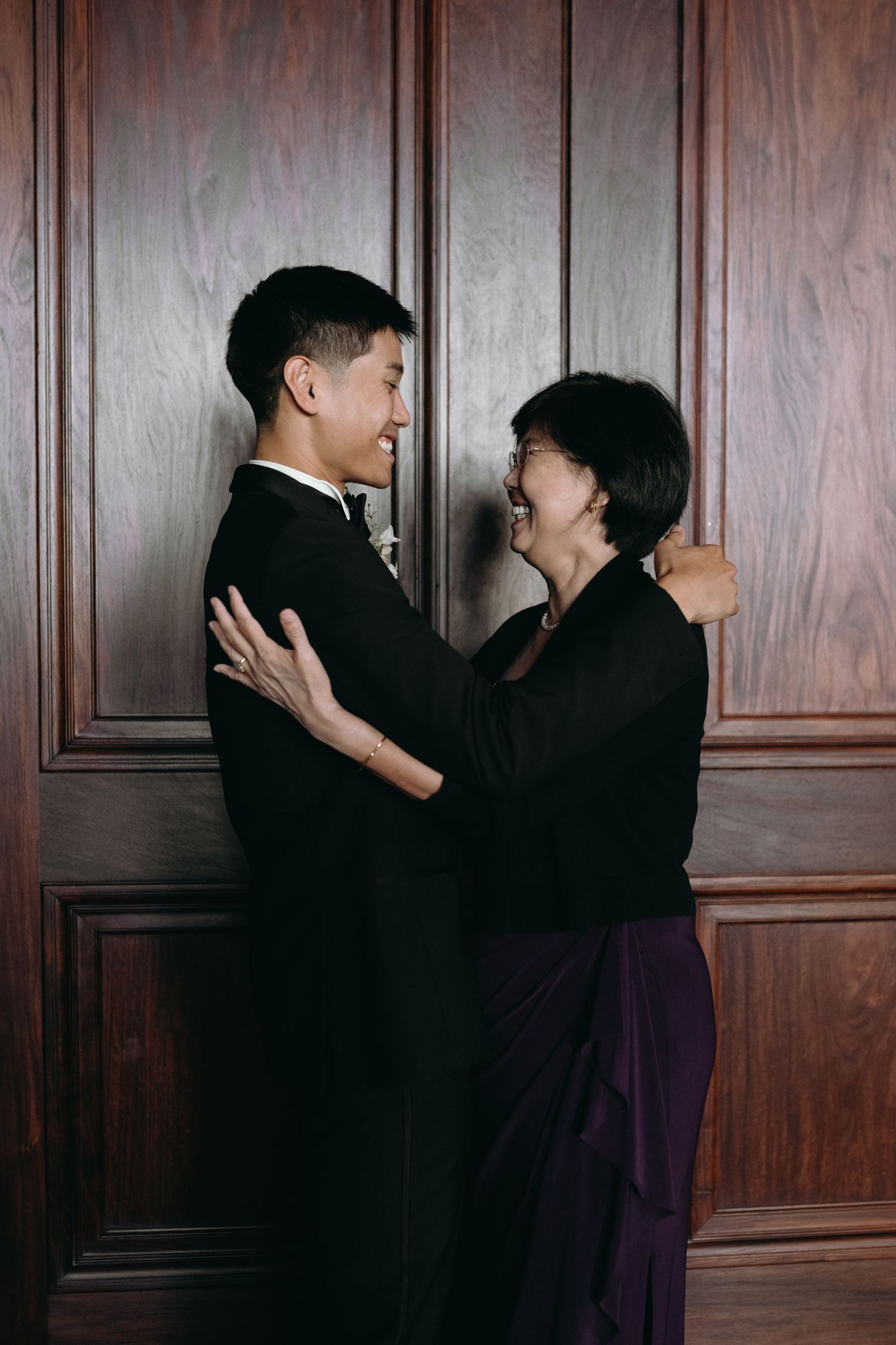 Intimate portrait of two people in formal attire sharing a moment against wooden paneled wall.