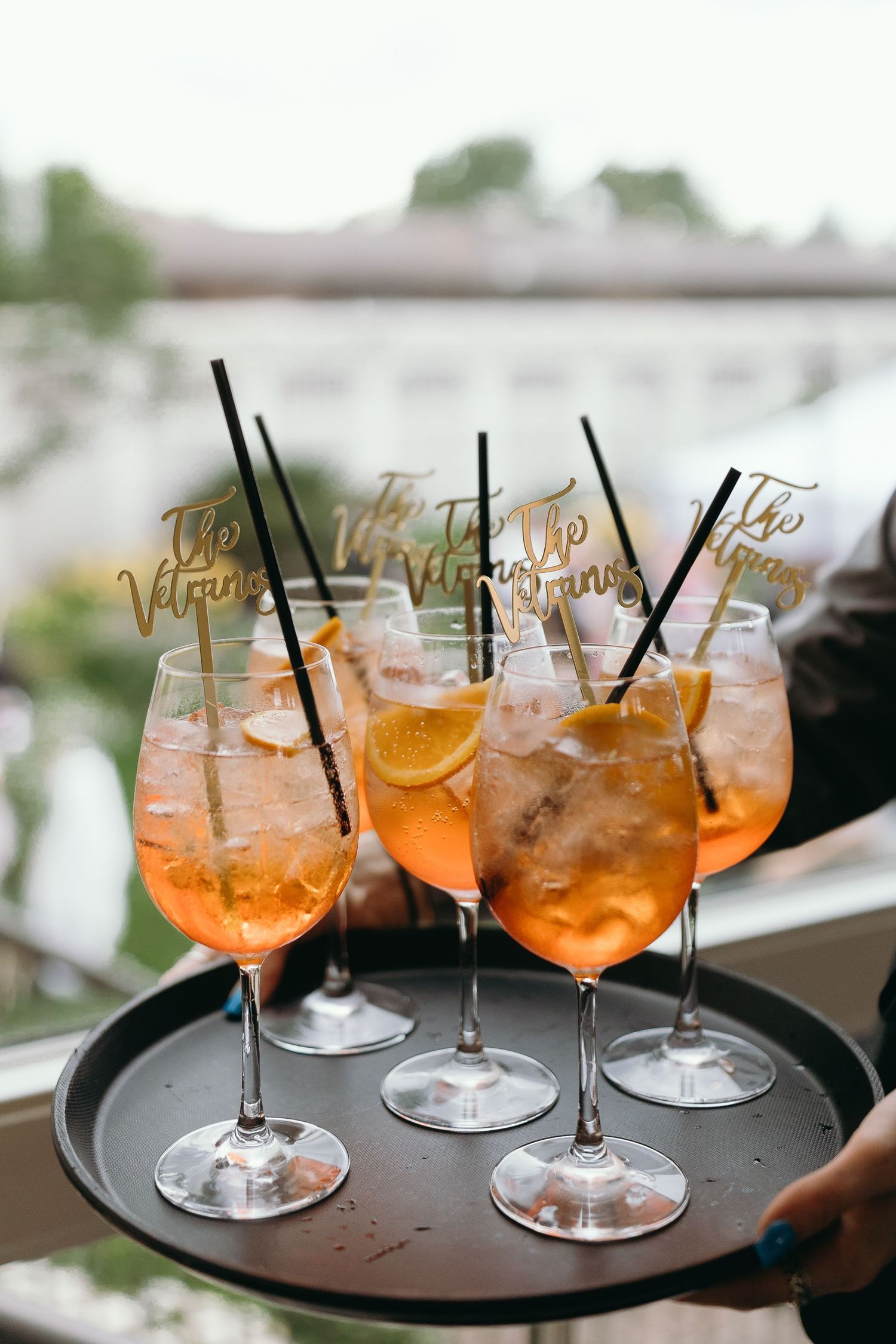 Aperol Spritz cocktails garnished with orange slices served on a round tray with decorative drink stirrers.