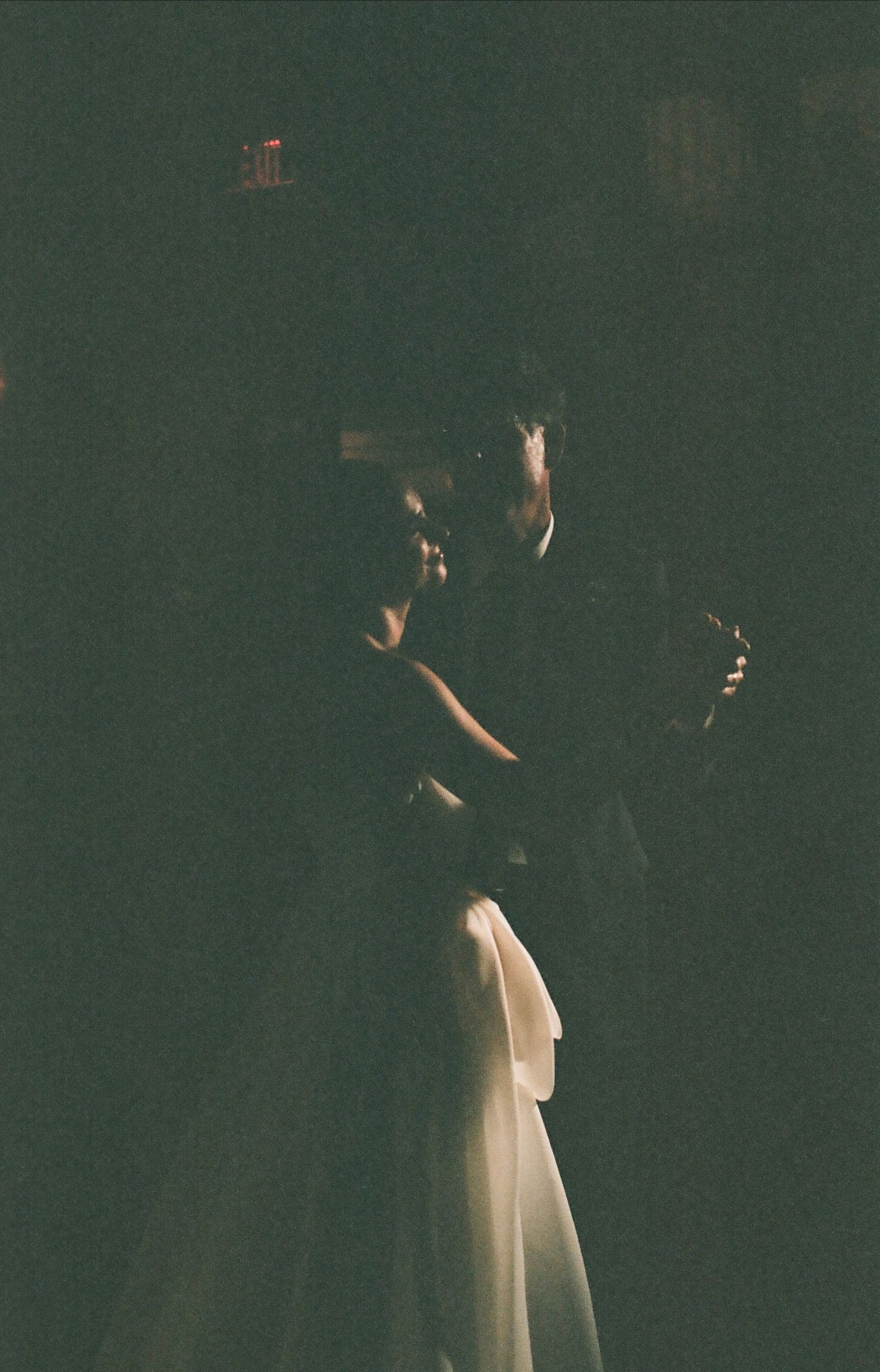 Dark moody silhouette of a dancing figure in flowing white fabric against a deep green background.