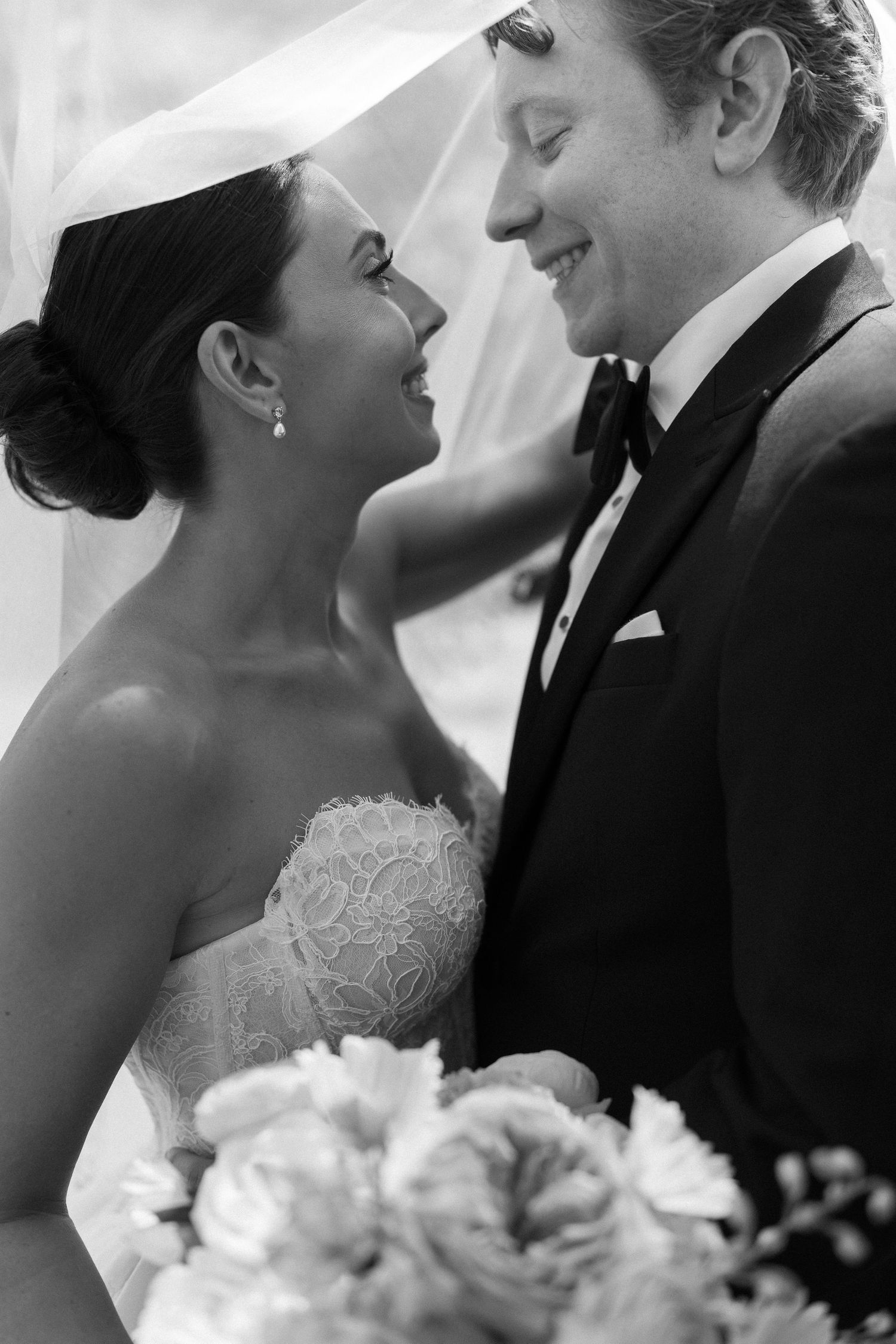 Black and white photo of a smiling bride and groom sharing an intimate moment under her wedding veil.