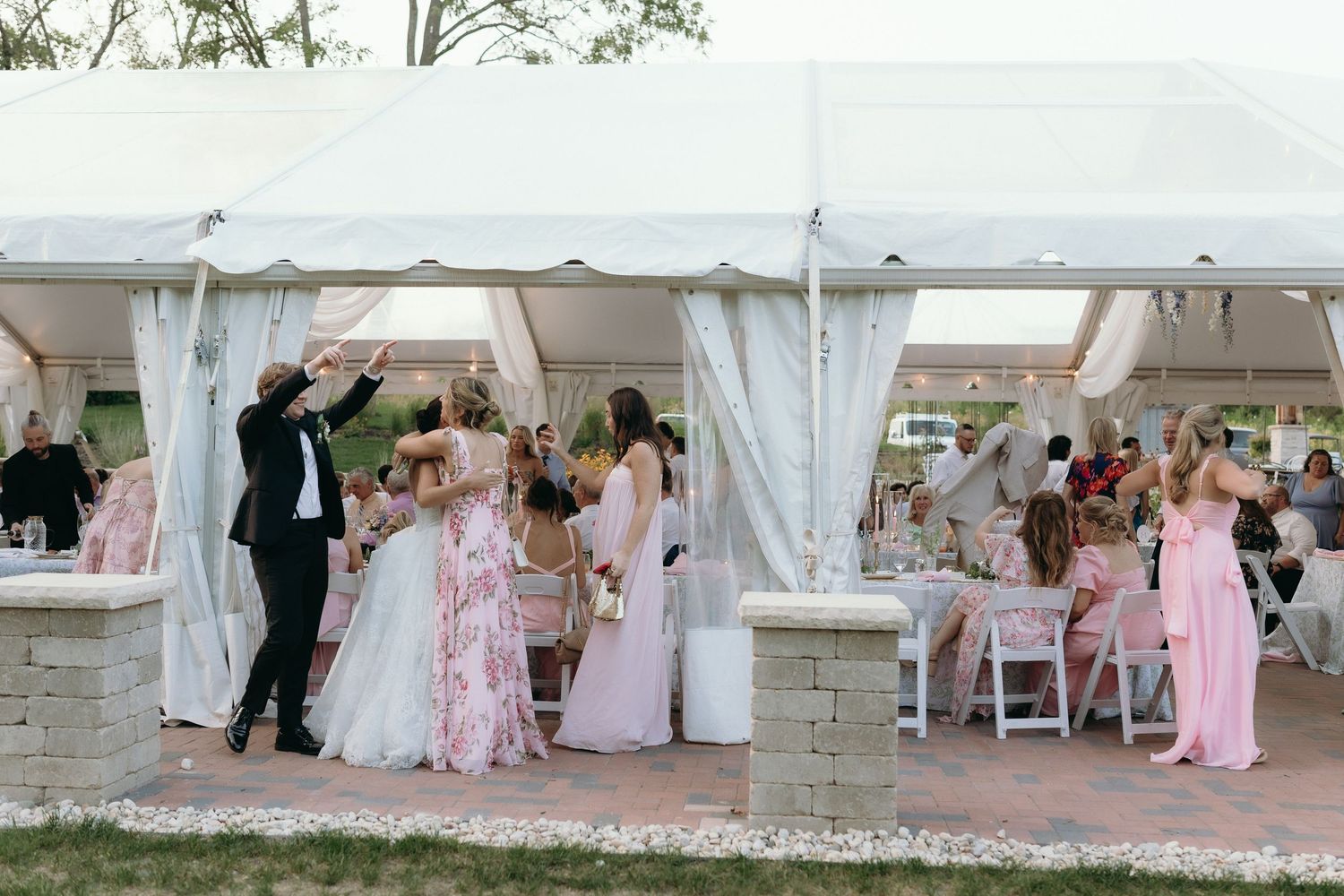 Wedding party celebrating under a white tent with bride, groom, and guests dancing outdoors.