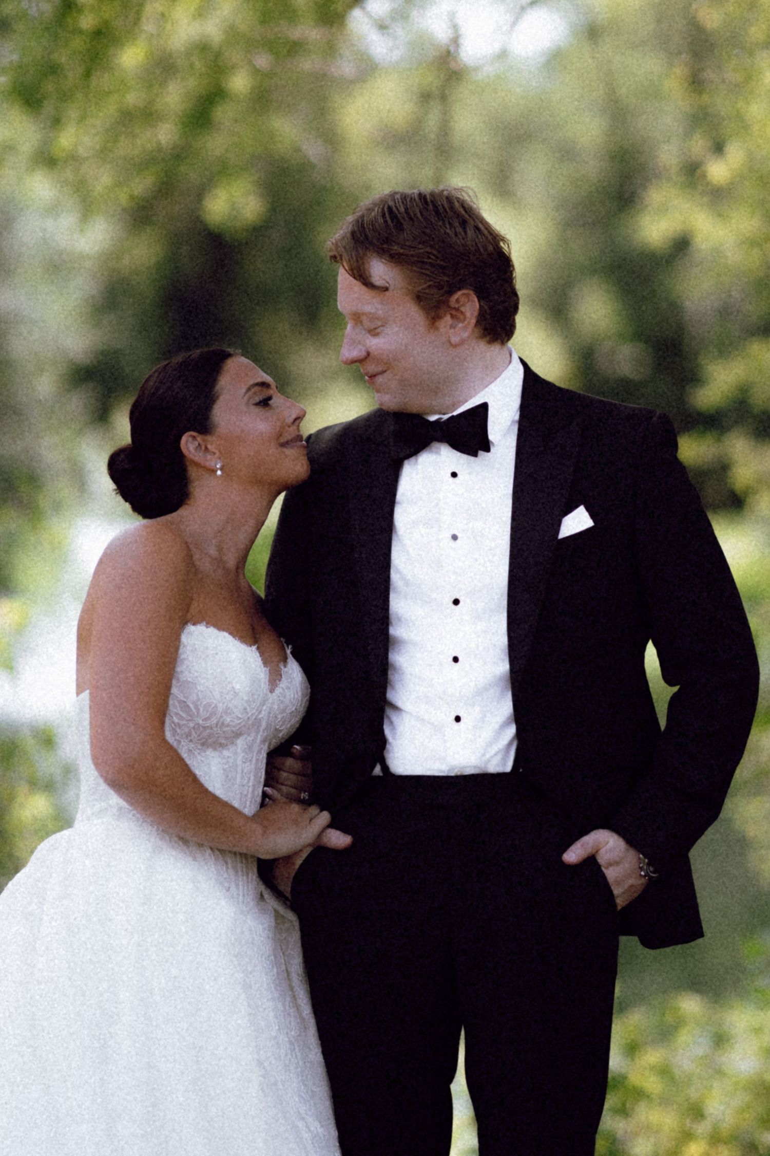 Bride and groom share romantic moment outdoors, she in strapless gown, he in black tuxedo.