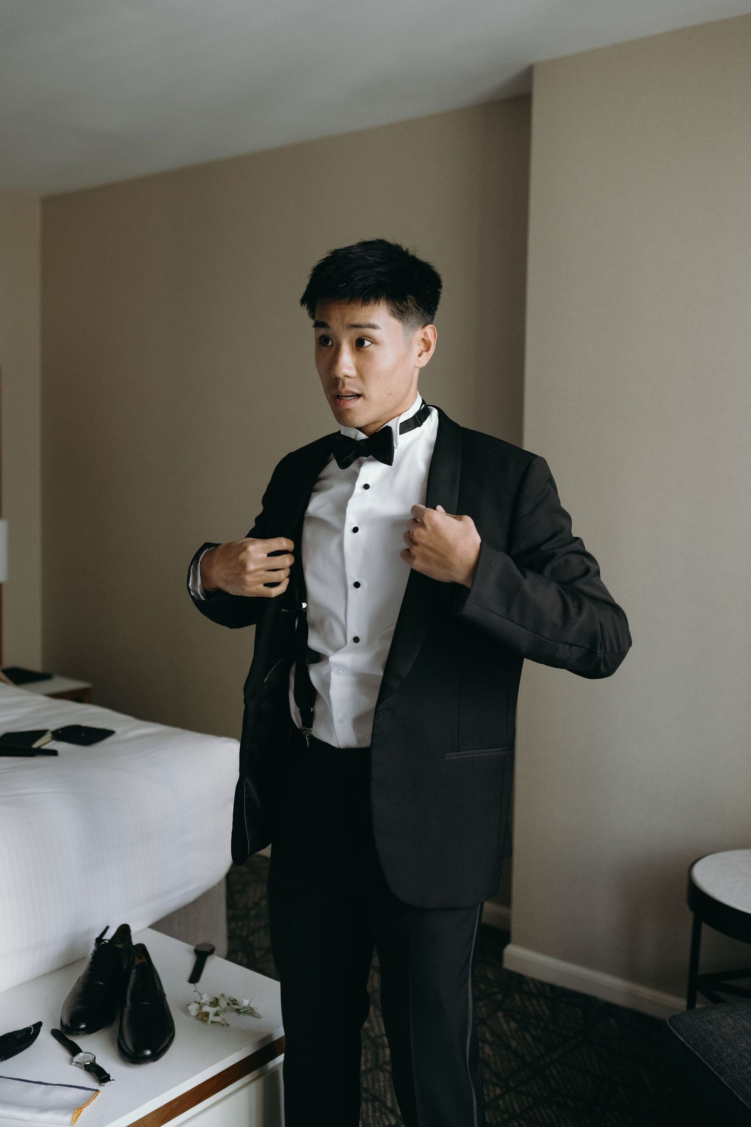 Groom adjusting black tuxedo and bow tie while getting ready.