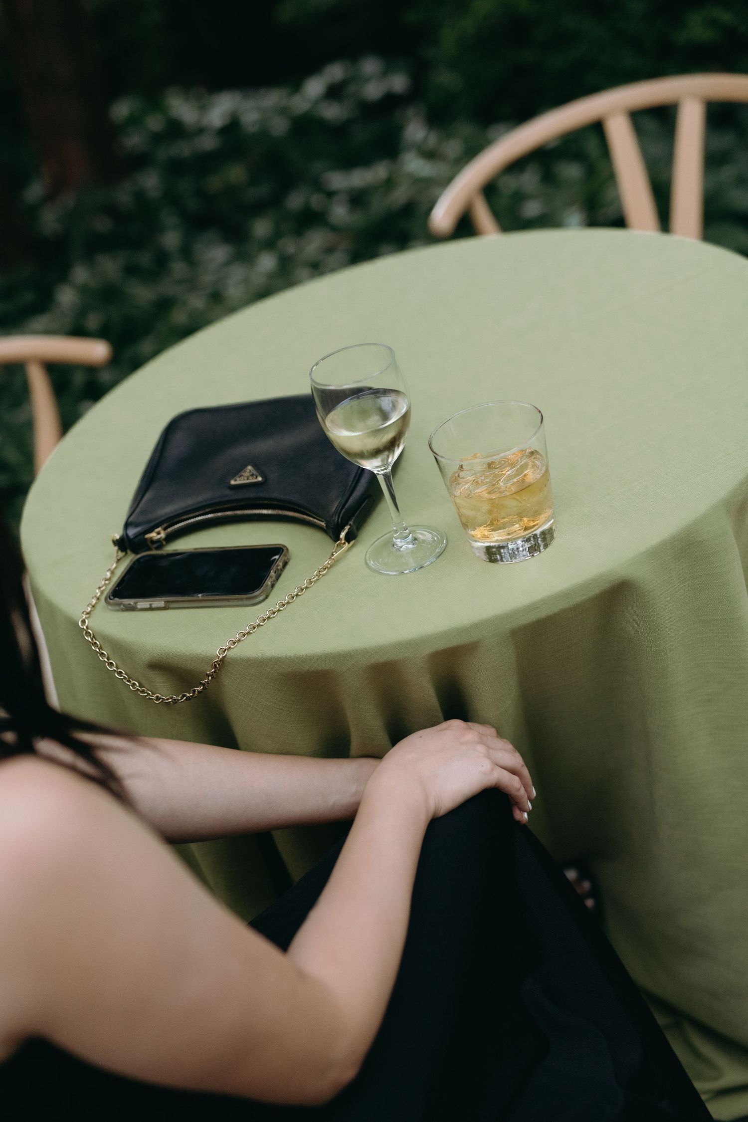 Table setting with drinks, purse and phone on sage green tablecloth.
