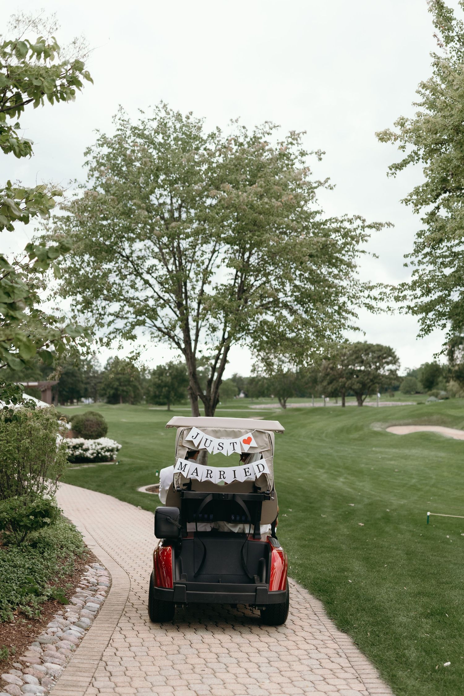 A decorated golf cart with 'Just Married' banner travels along a winding path on a golf course.
