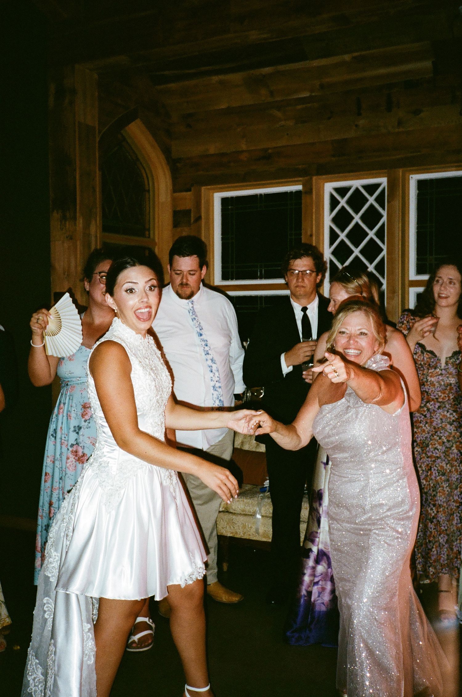 Bride and guest dancing joyfully at a rustic wedding reception with guests watching in the background.