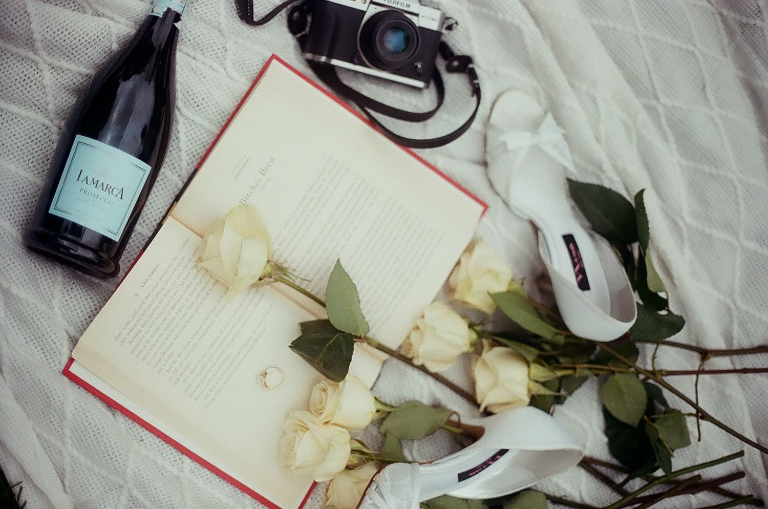 Styled flat lay with white roses, perfume bottles, and white lace fabric creating an elegant composition.