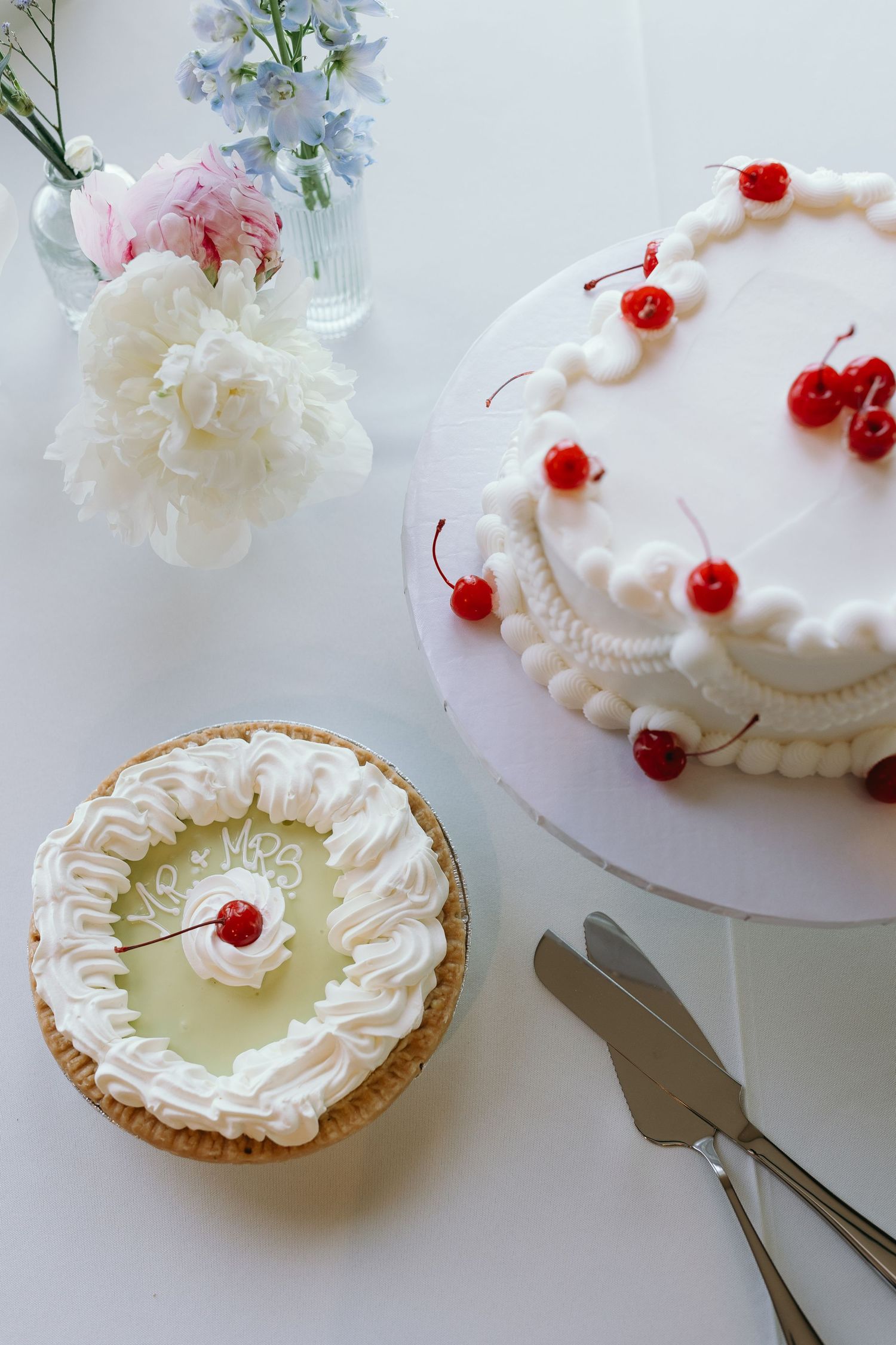 A delicate arrangement of cakes, including a white frosted cake with red cherries and a mini pie with whipped cream topping.