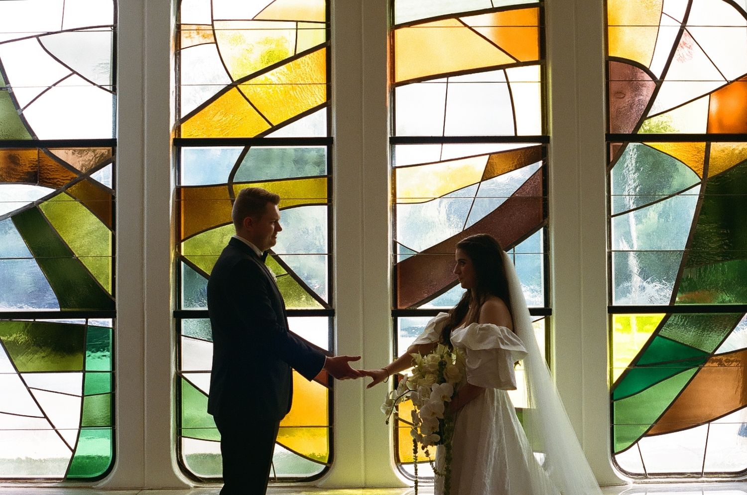 Couple exchanges vows in front of stunning stained glass windows in a church wedding ceremony.