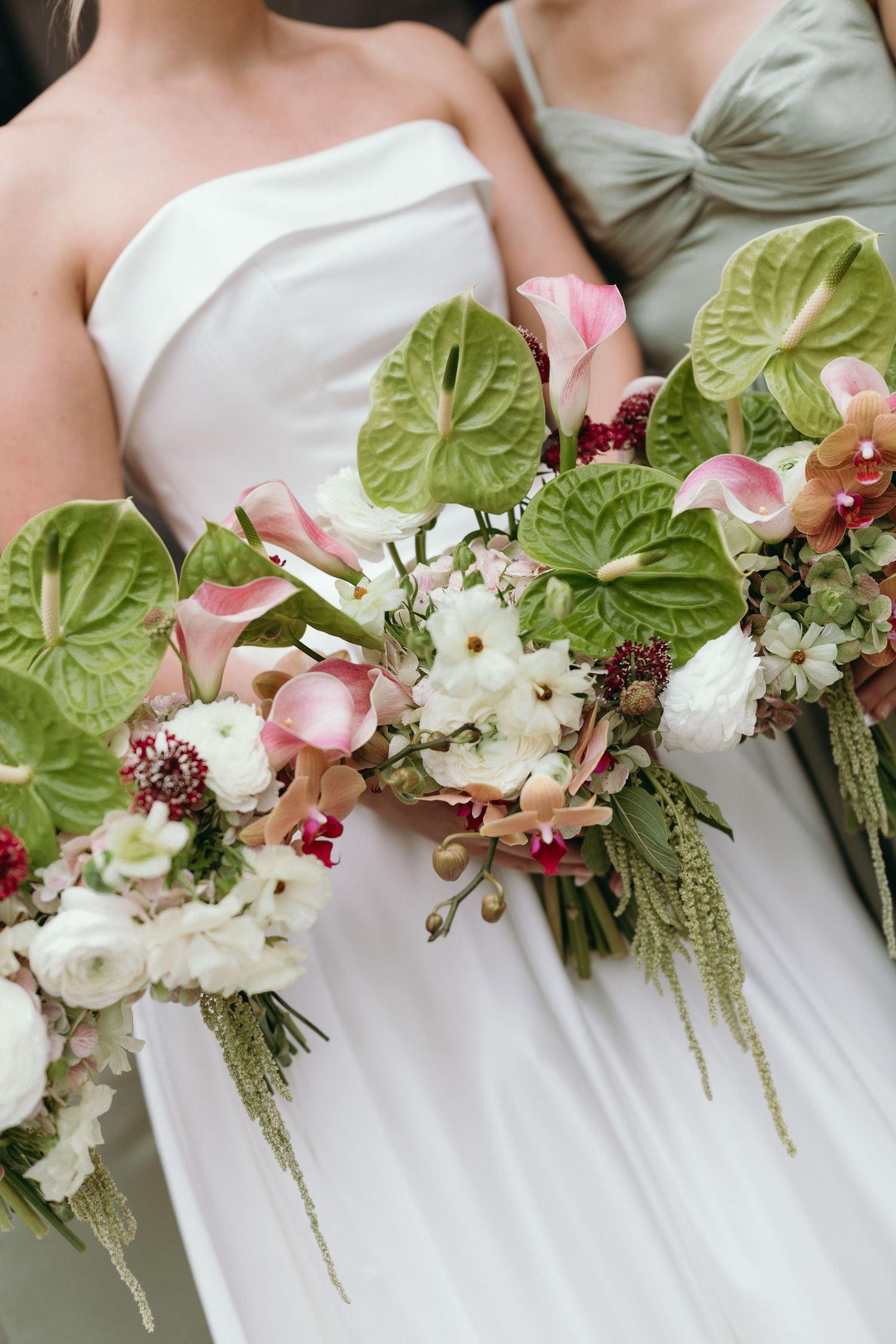 Wedding bouquets featuring pink and white flowers with large green leaves arranged in a row against white dresses.