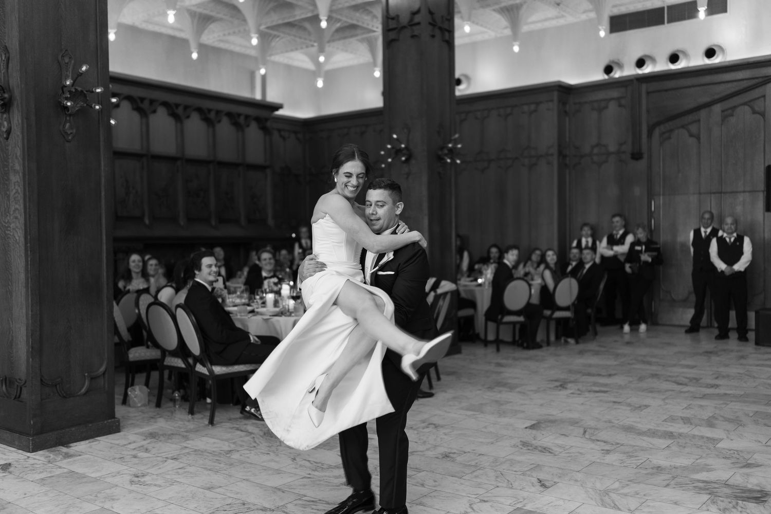 Groom lifting bride during first dance in elegant black and white wedding reception photo.