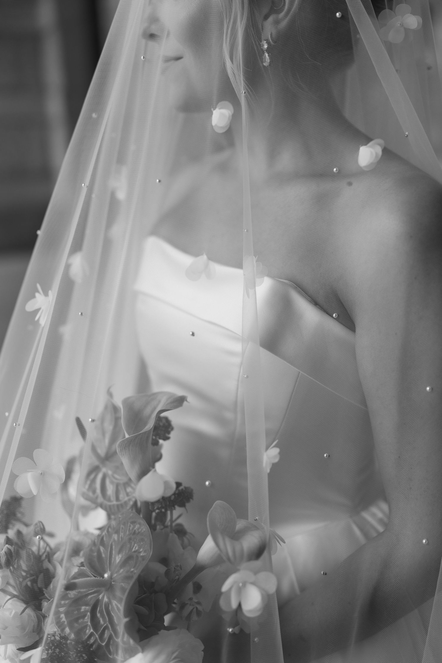 Elegant black and white bridal portrait showing strapless wedding dress, delicate veil, and floral bouquet details.
