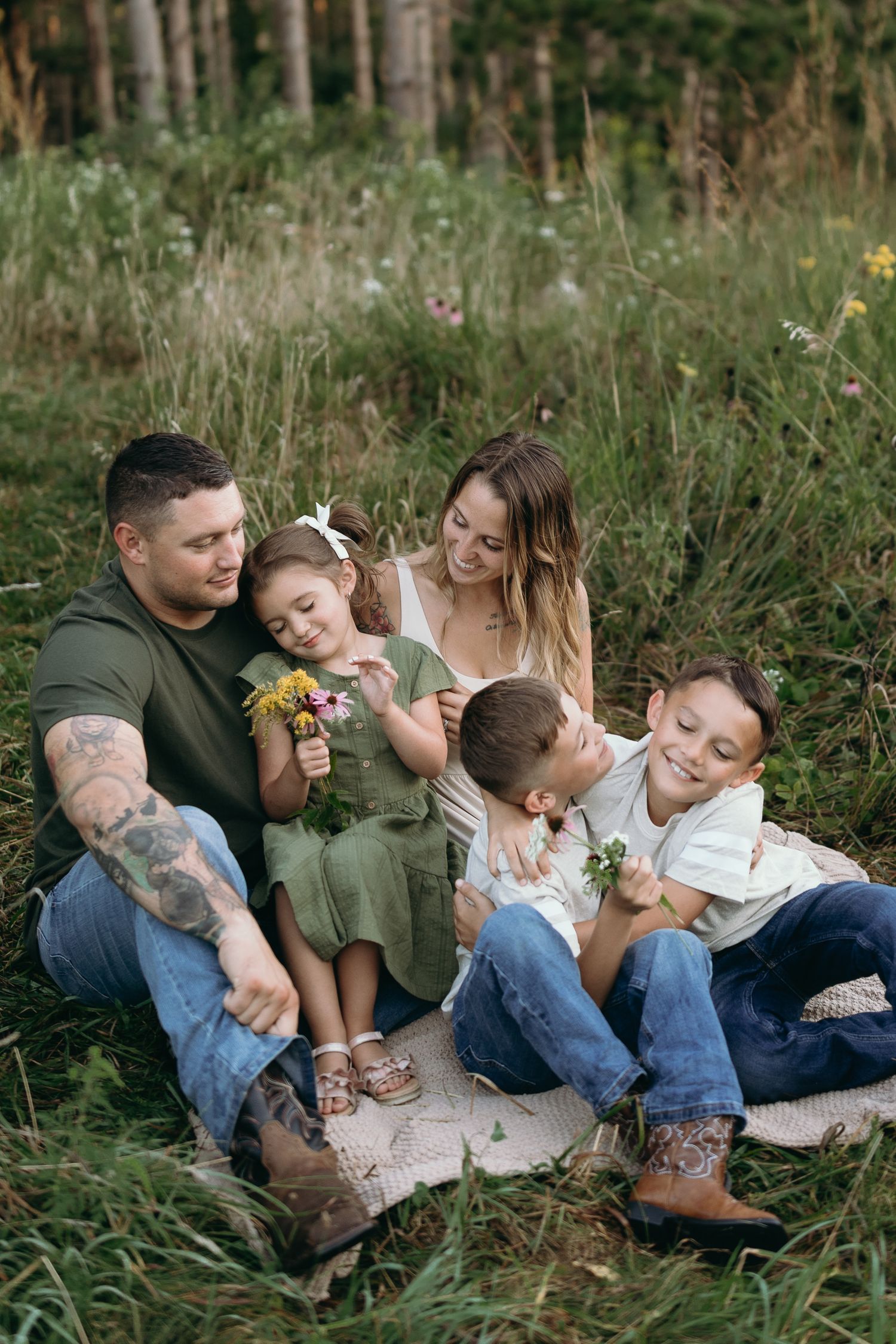 Family sitting together on a blanket in tall grass during an outdoor photo session in nature.