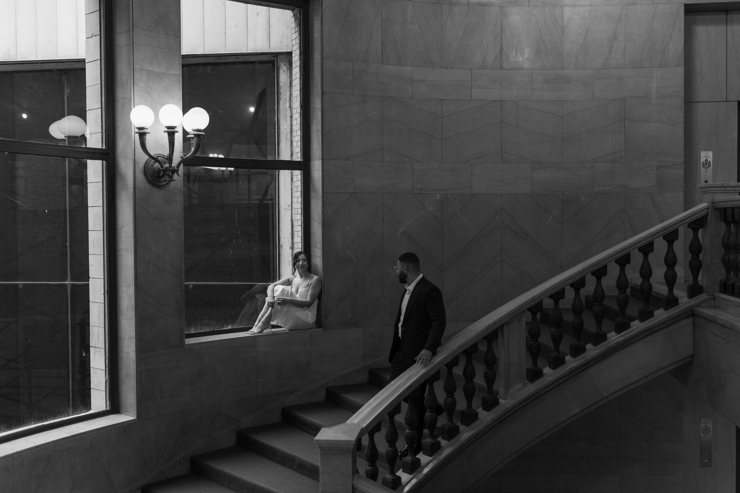 Artistic black and white photo of couple on grand staircase in elegant building.