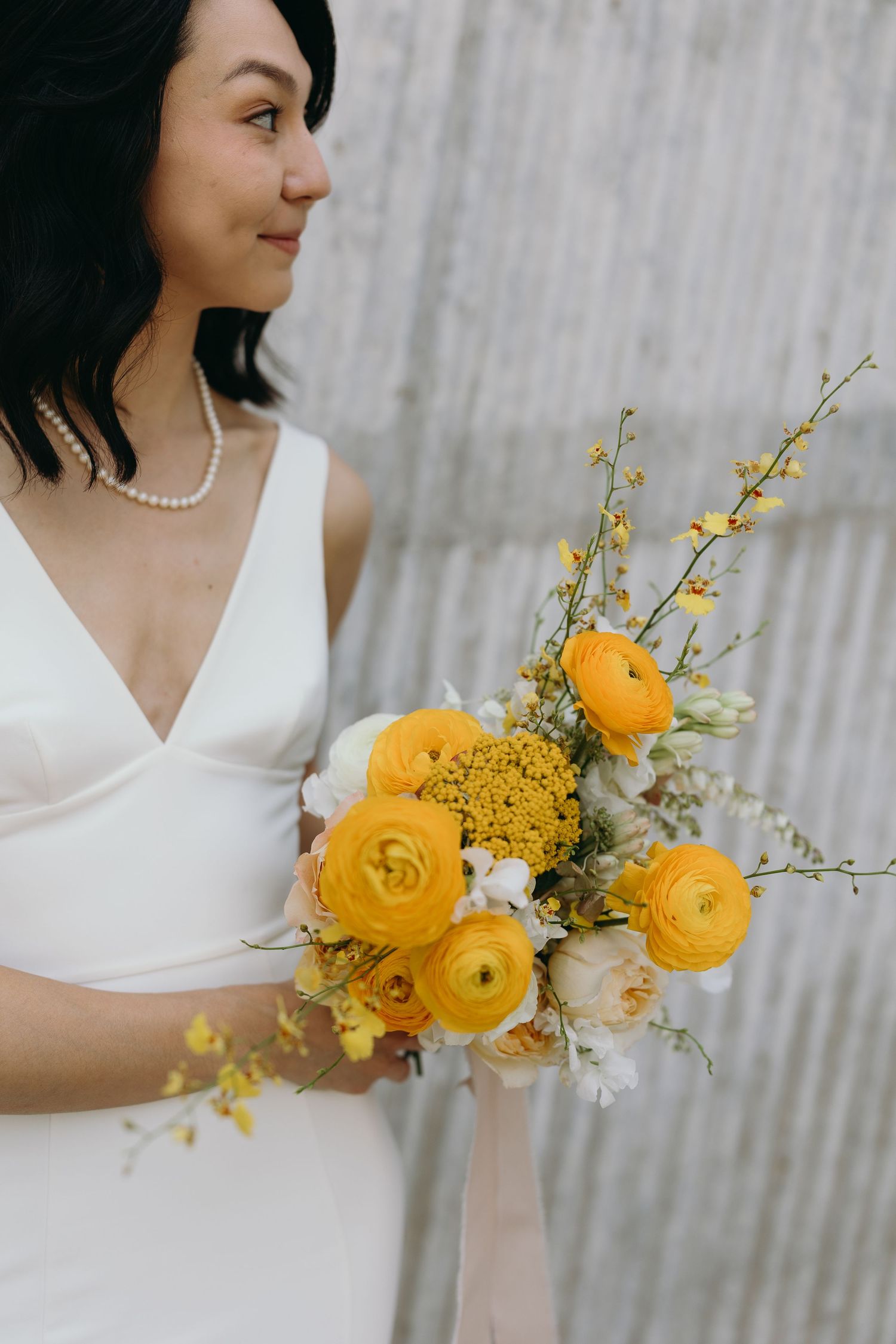 Bright yellow ranunculus flowers arranged in an elegant bridal bouquet with white accents.