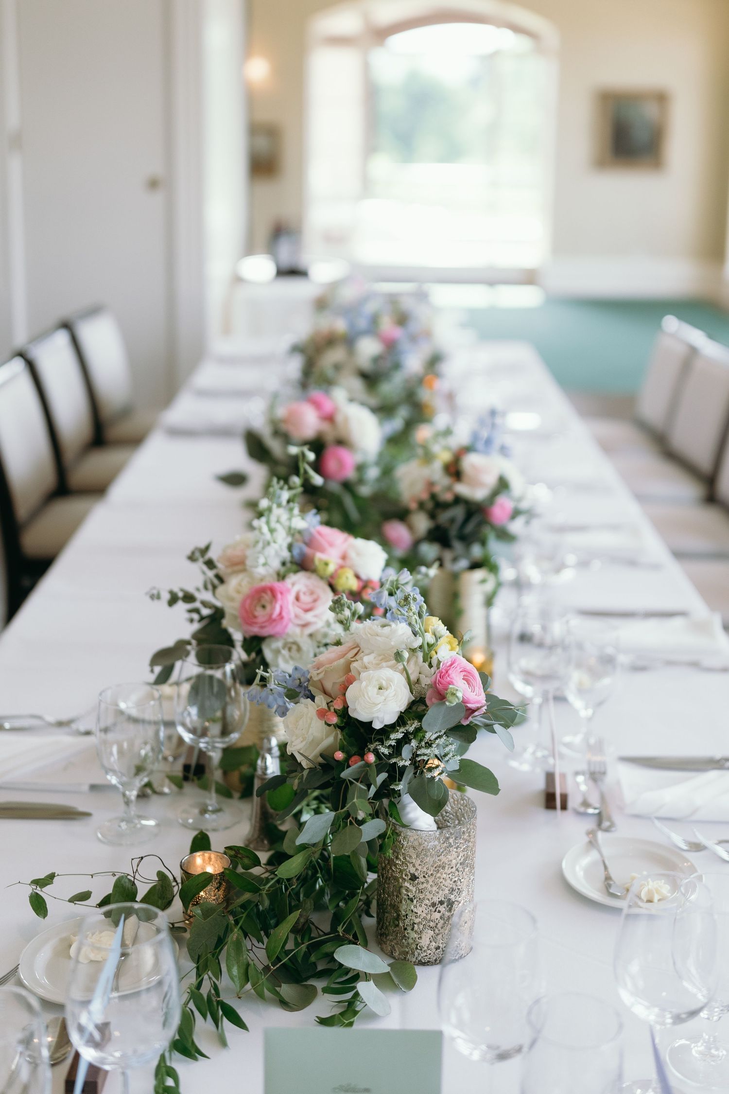 Long dining table decorated with romantic floral centerpieces and glassware.