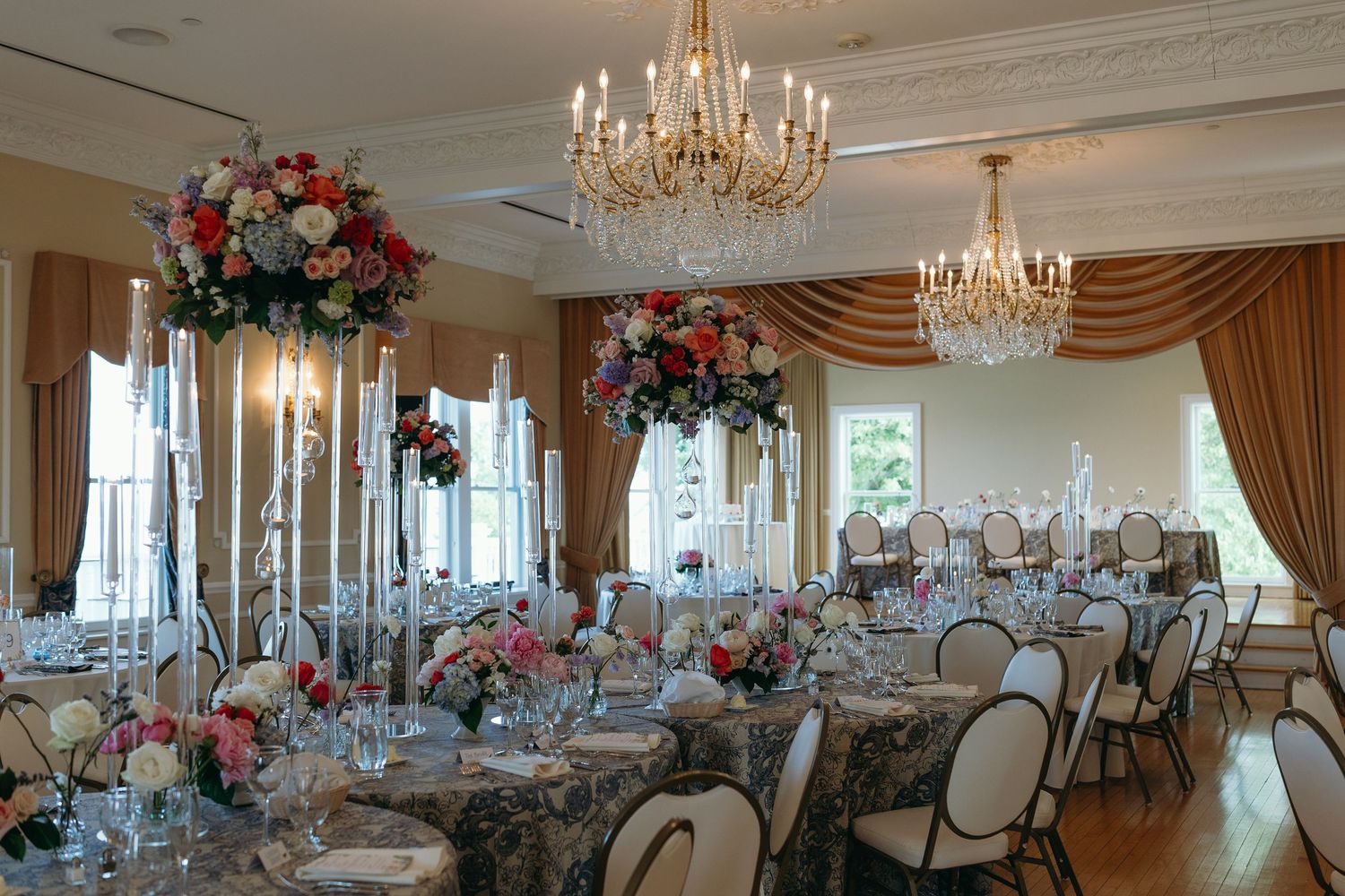 Elegant ballroom reception setup with crystal chandeliers and tall floral centerpieces.