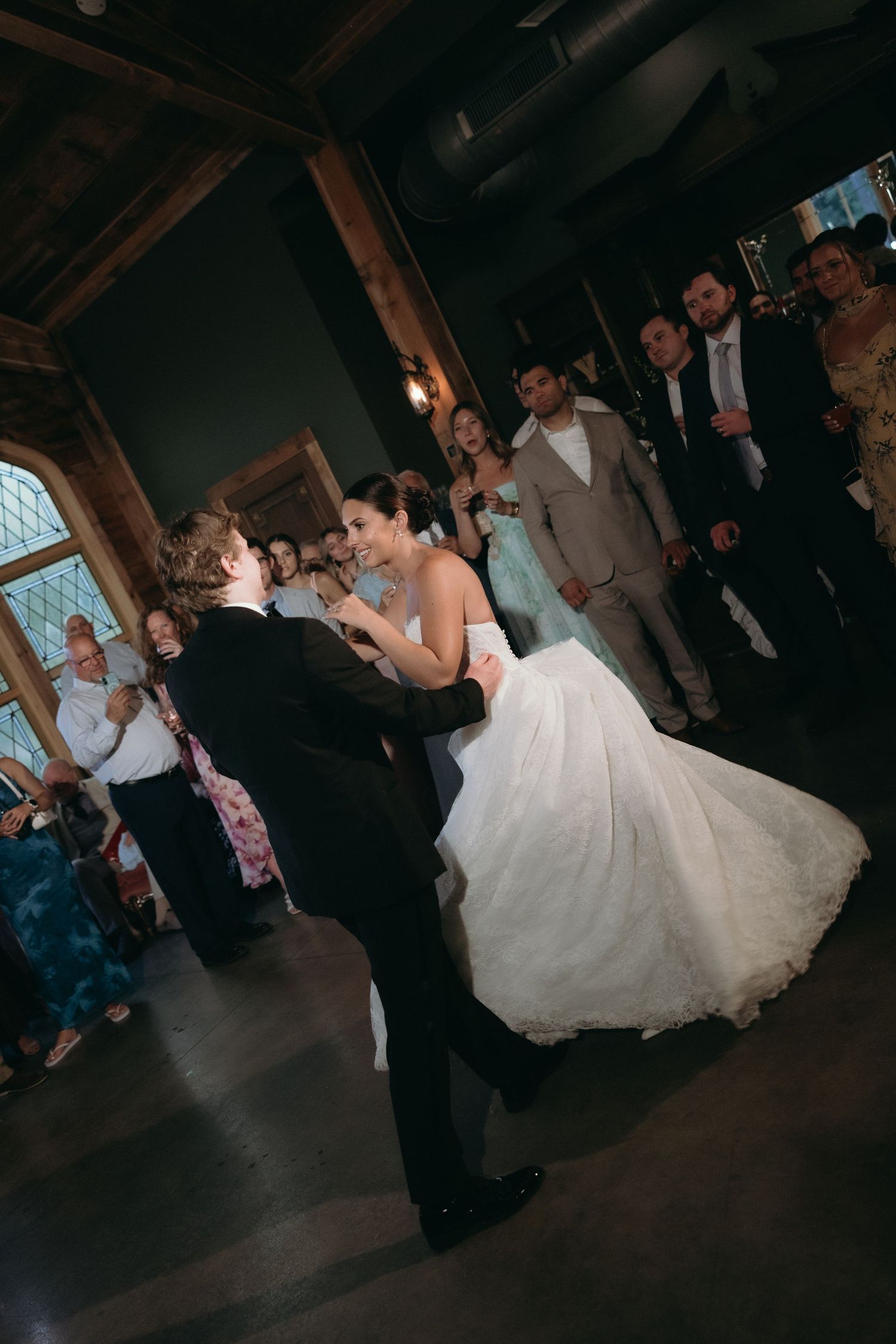 Bride and groom share their first dance surrounded by wedding guests in an elegant rustic venue.