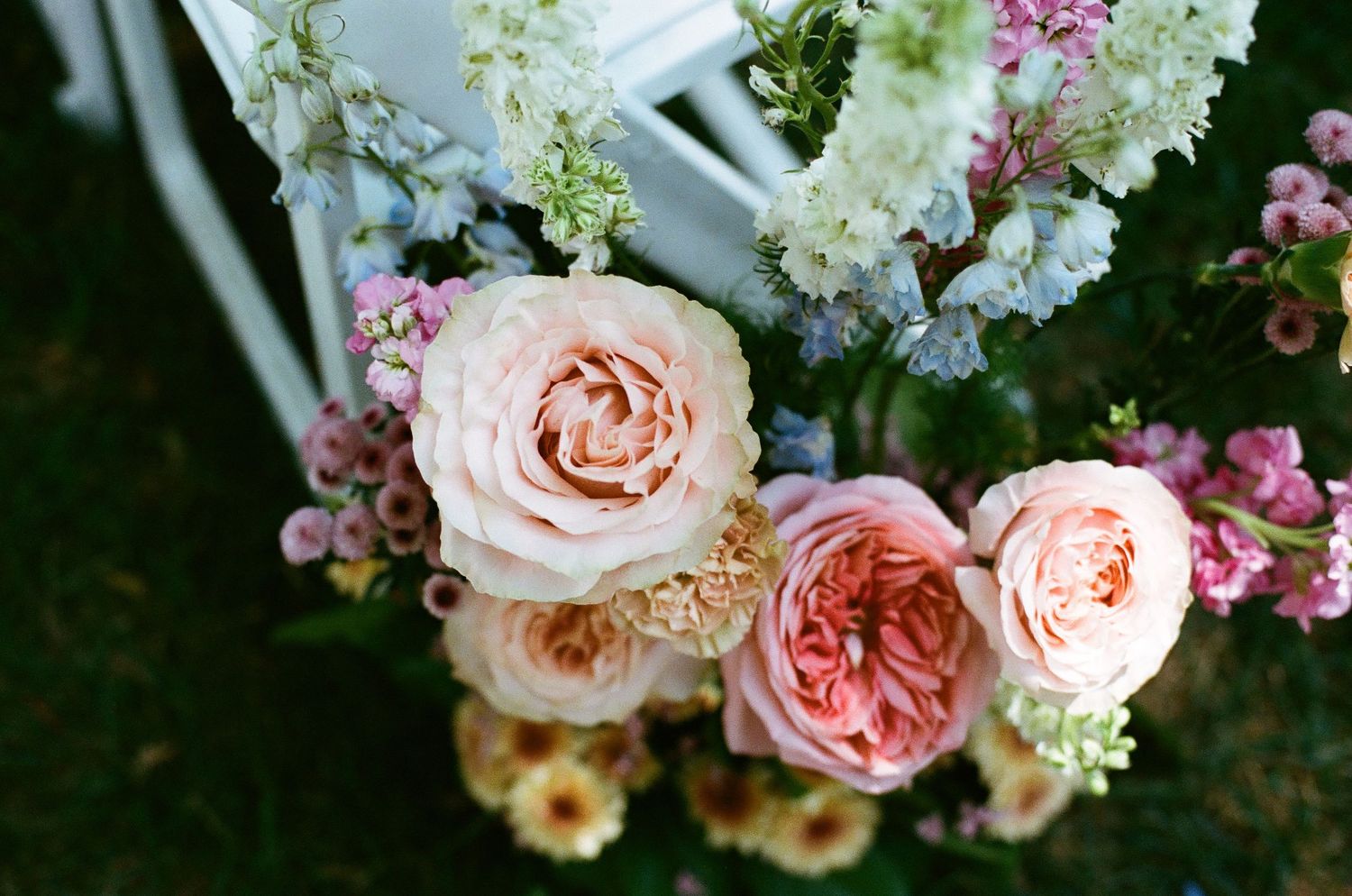 Elegant wedding floral arrangement featuring blush pink garden roses and mixed blooms on a white chair.