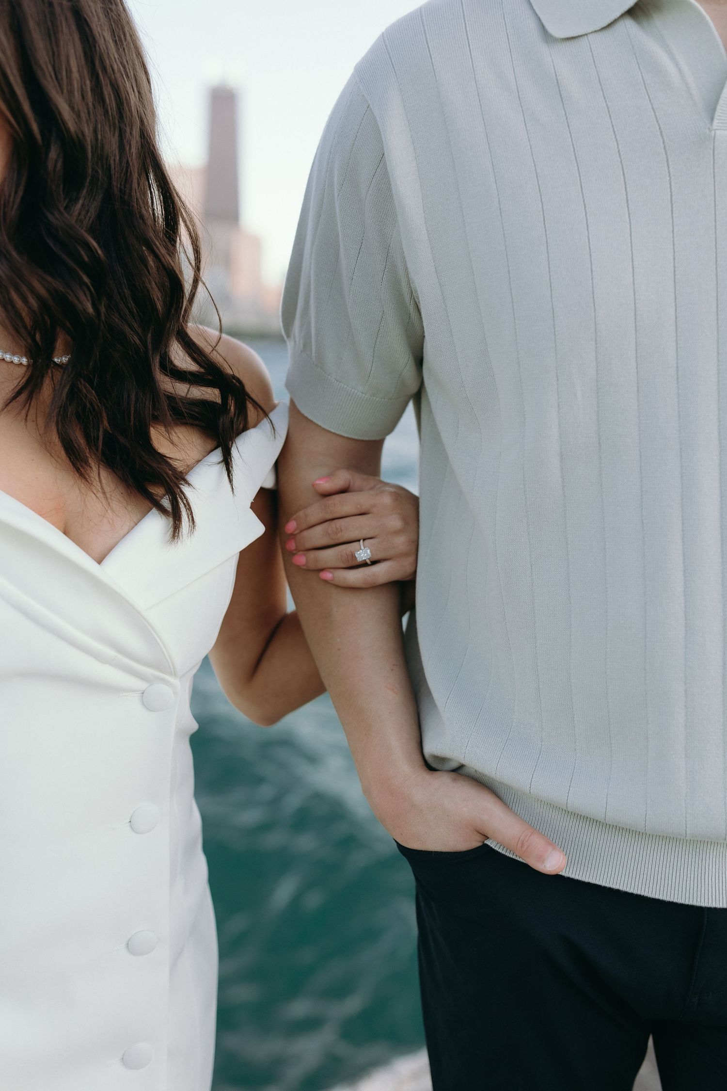 Close-up of couple holding hands, showing wedding ring detail against white clothing and blurred urban backdrop.