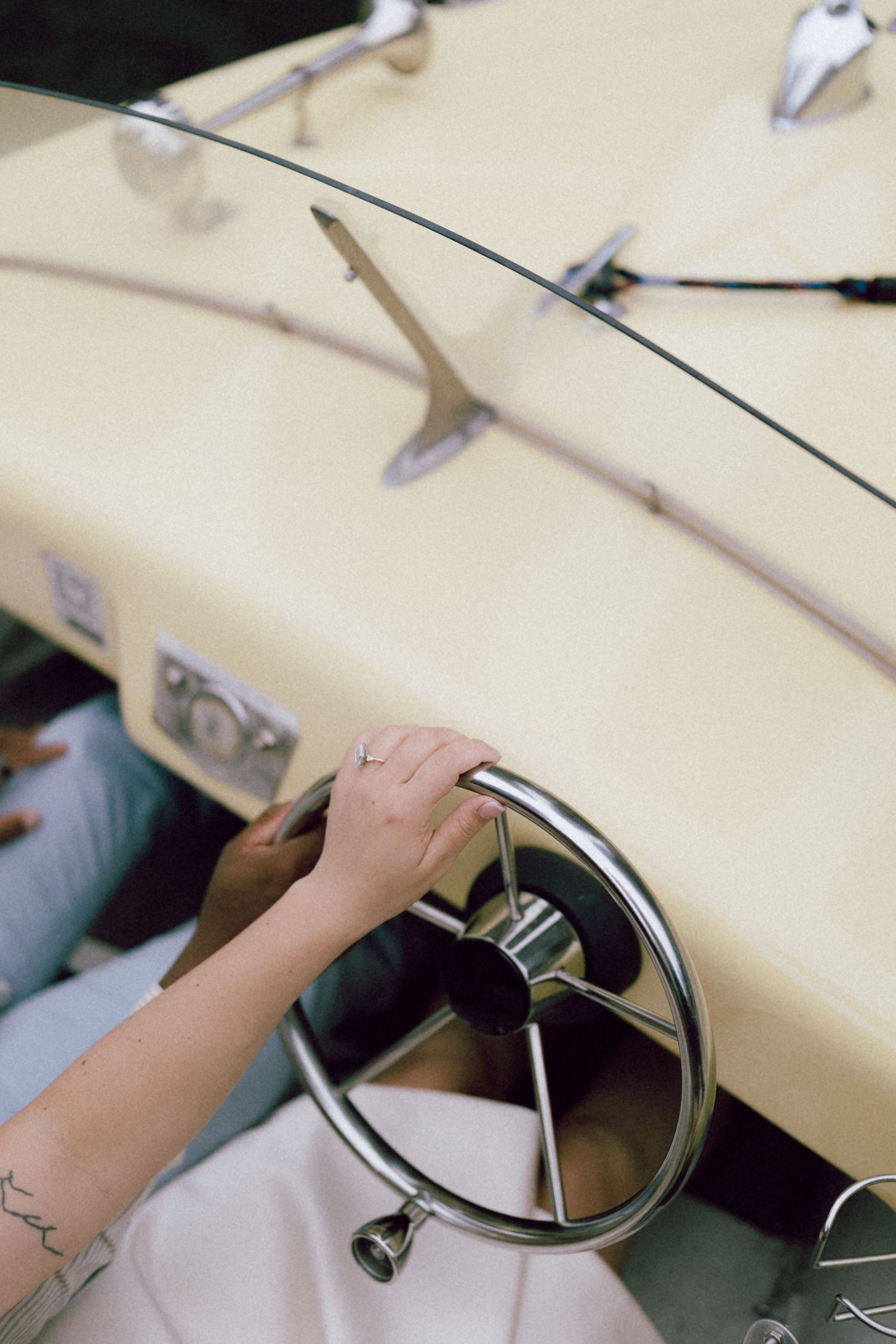 Close-up of a hand on a chrome steering wheel of a vintage cream-colored boat.