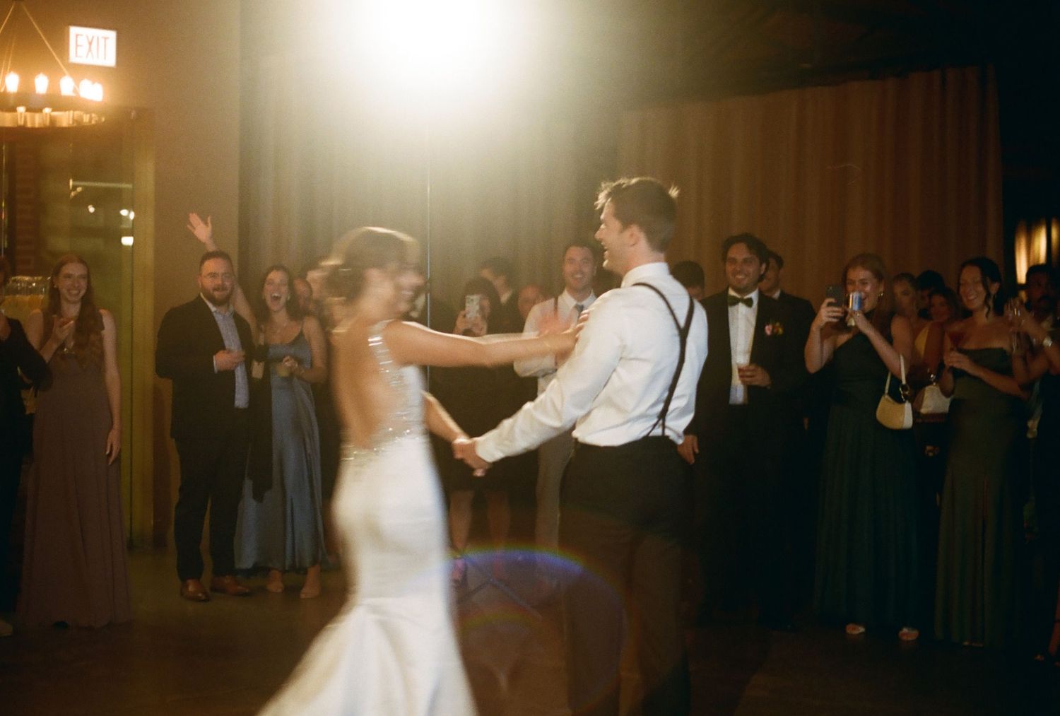 Bride and groom share their first dance at a romantic wedding reception with guests watching in the background.