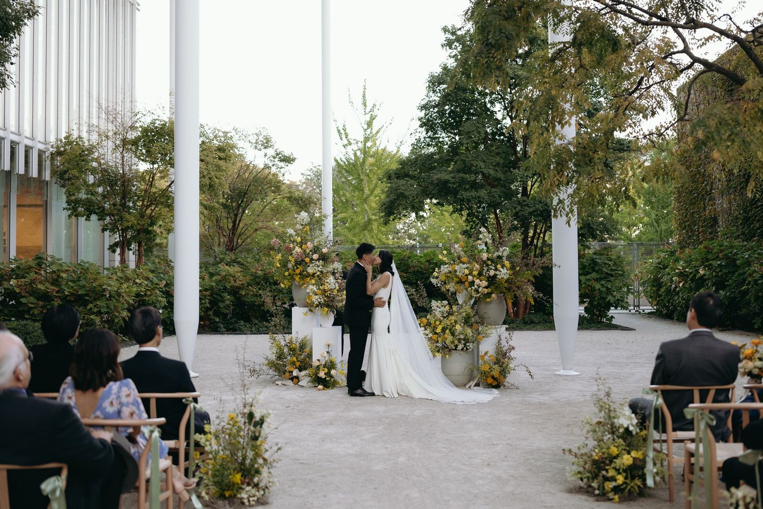 Outdoor wedding ceremony setup with white pillars and floral arrangements along a garden path.