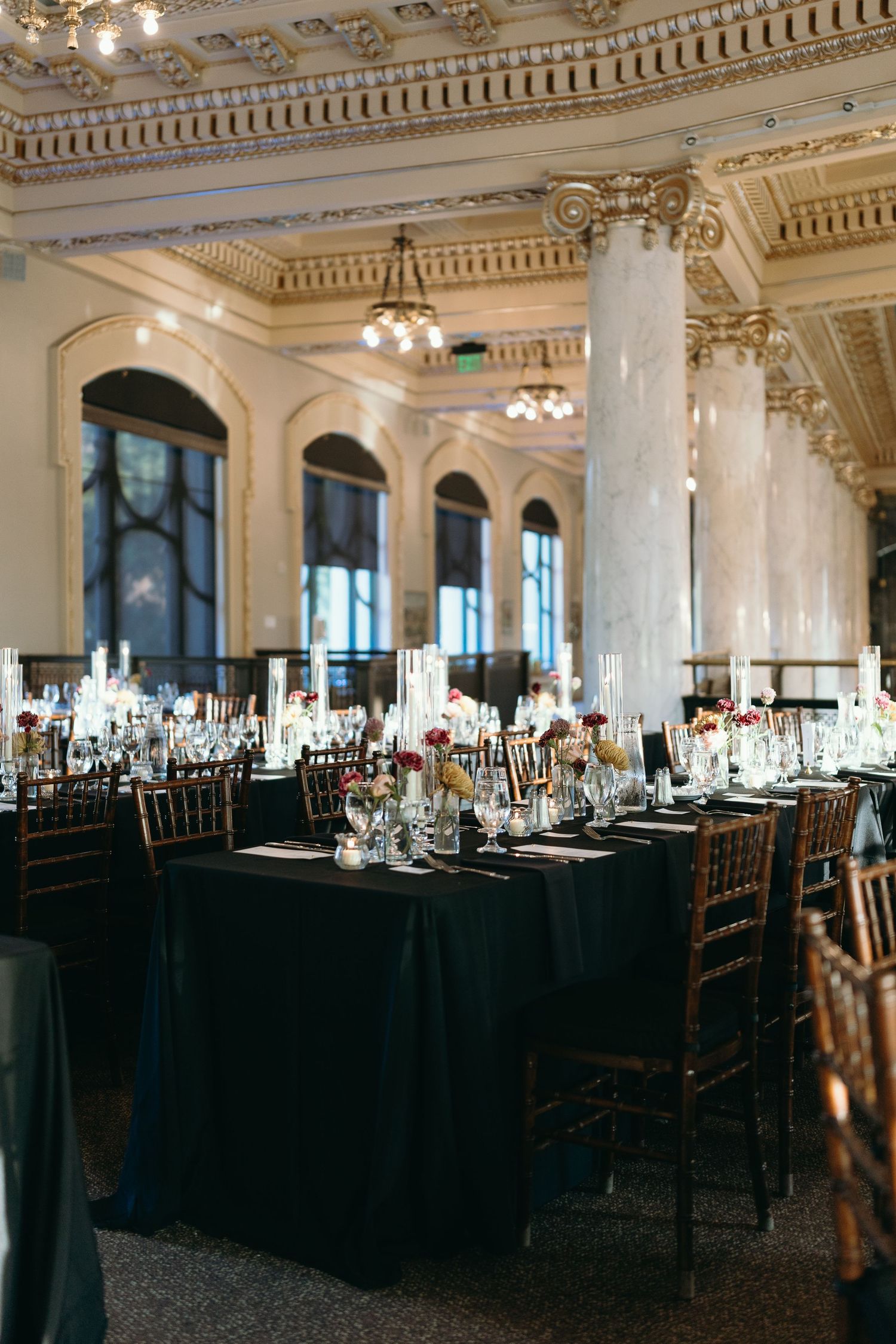 Reception tables set with black linens and chiavari chairs in an ornate ballroom with columned architecture.
