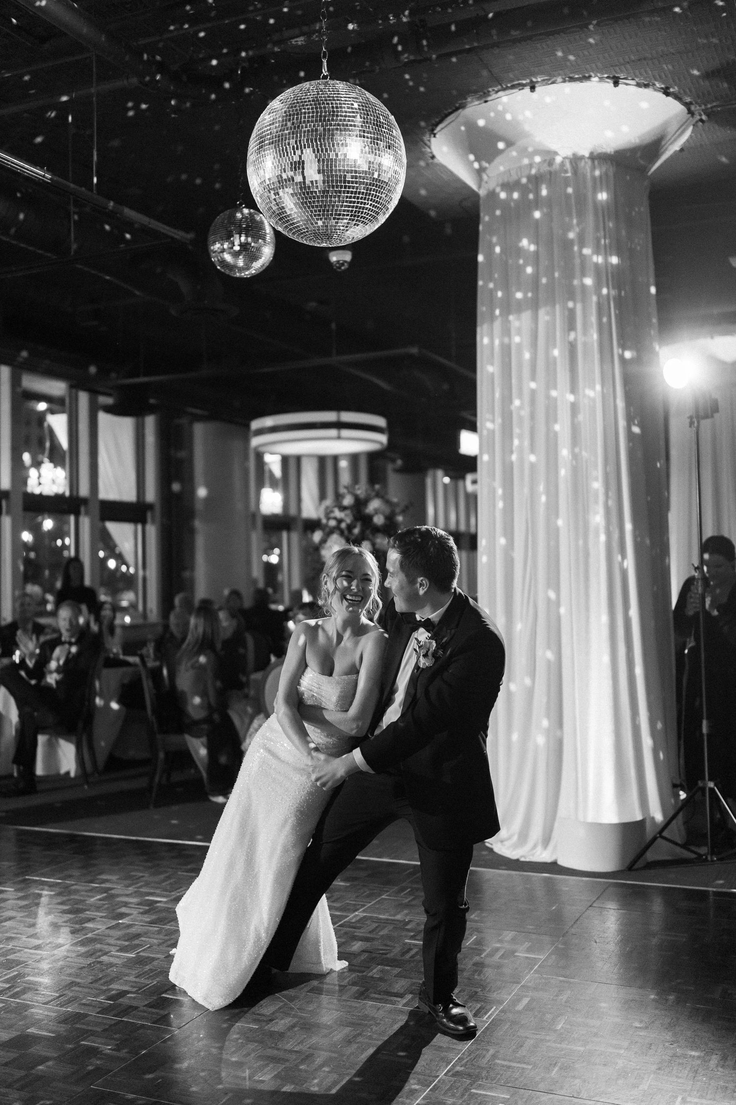 Dramatic wedding dance scene with disco balls and illuminated drapery in a dark reception venue.