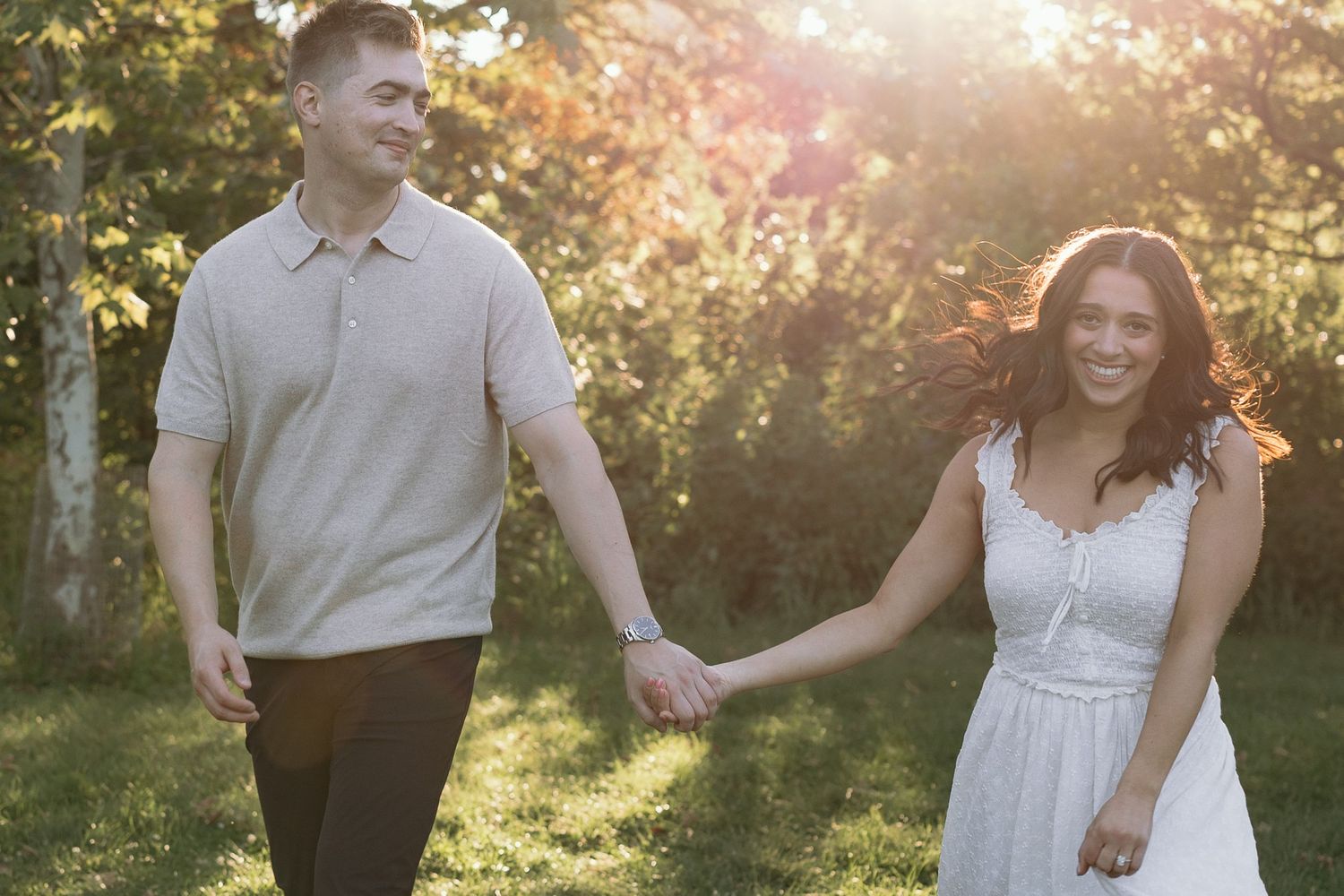 Couple holding hands and walking together in a sunlit garden during golden hour.