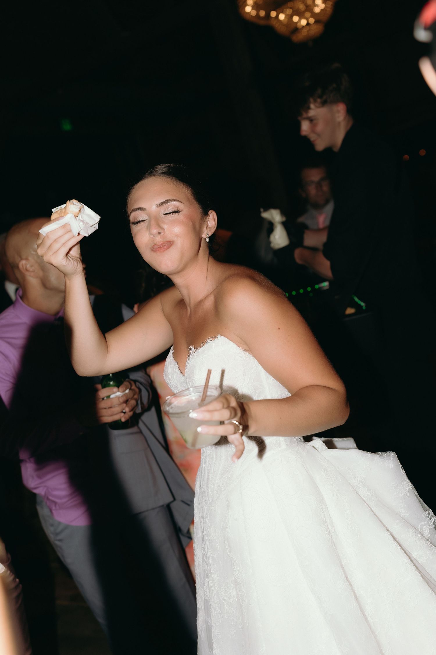 Bride in white gown dancing joyfully with cash at lively wedding reception party.