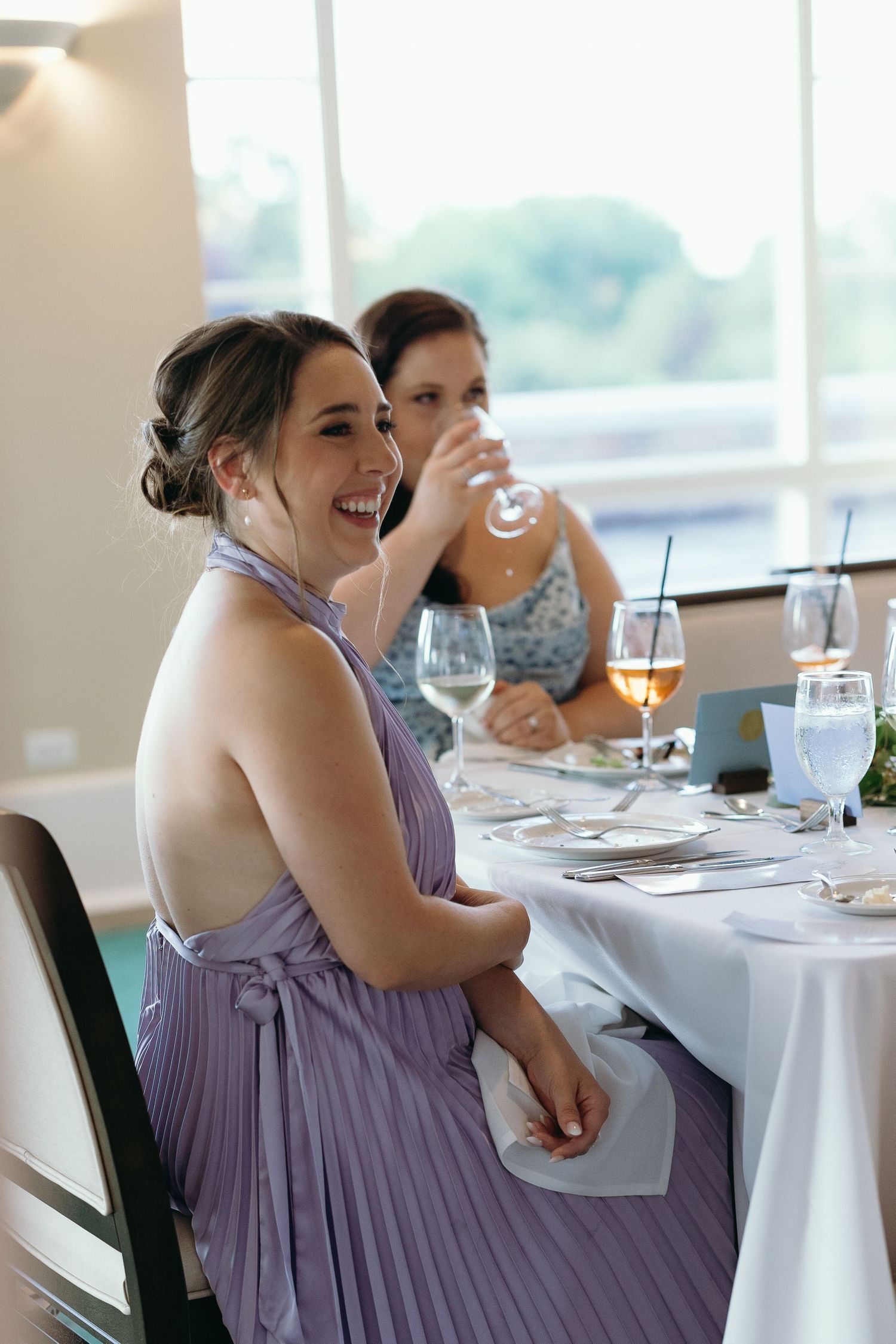 Woman in purple bridesmaid dress laughing during reception dinner.