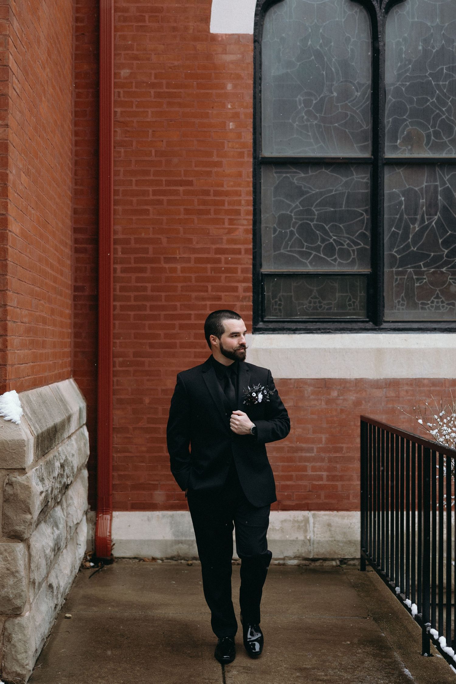 Several people in black clothing walk along a red brick exterior corridor with railings.