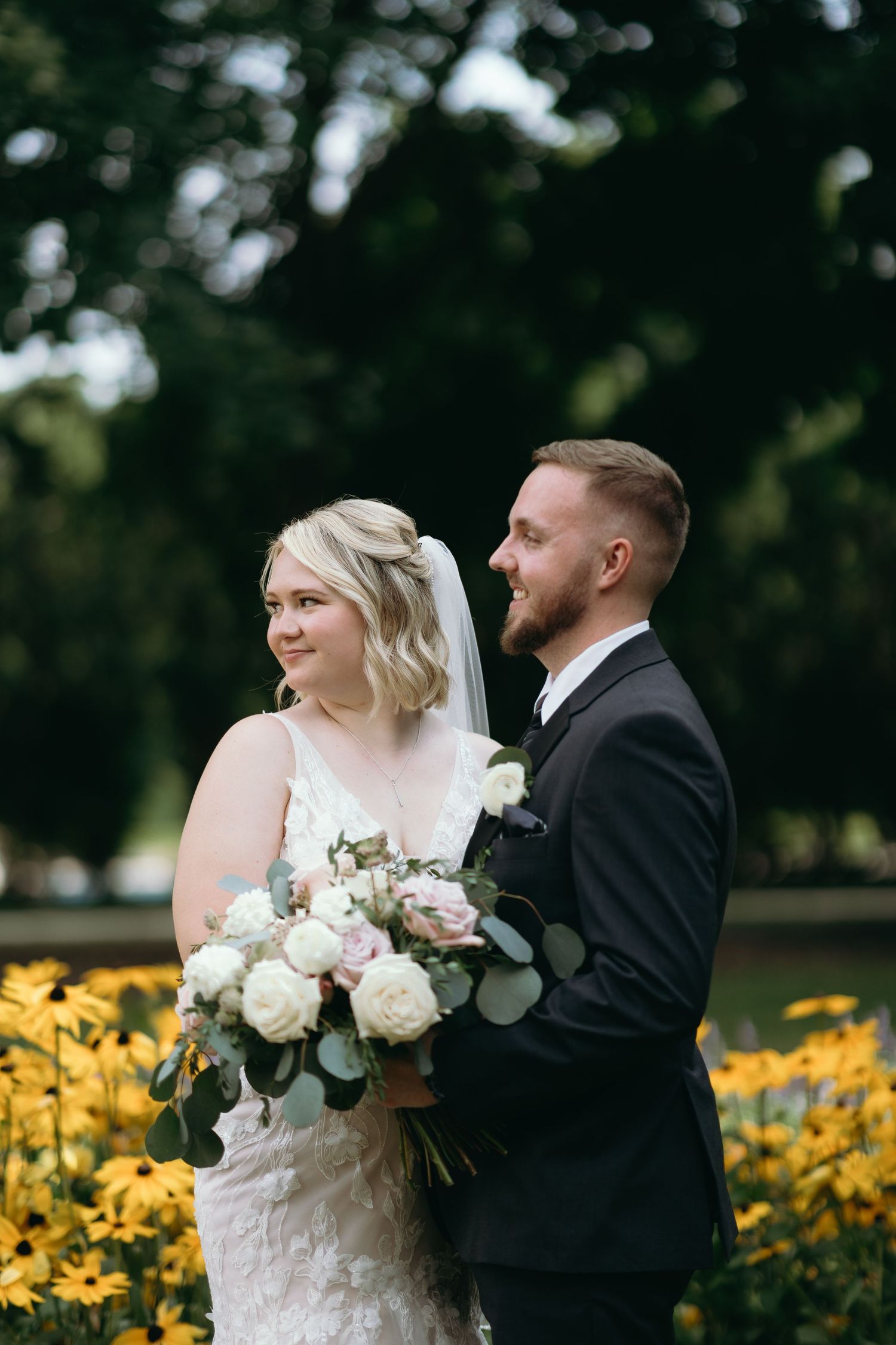 Newlyweds share a joyful moment in a garden with blooming yellow flowers.