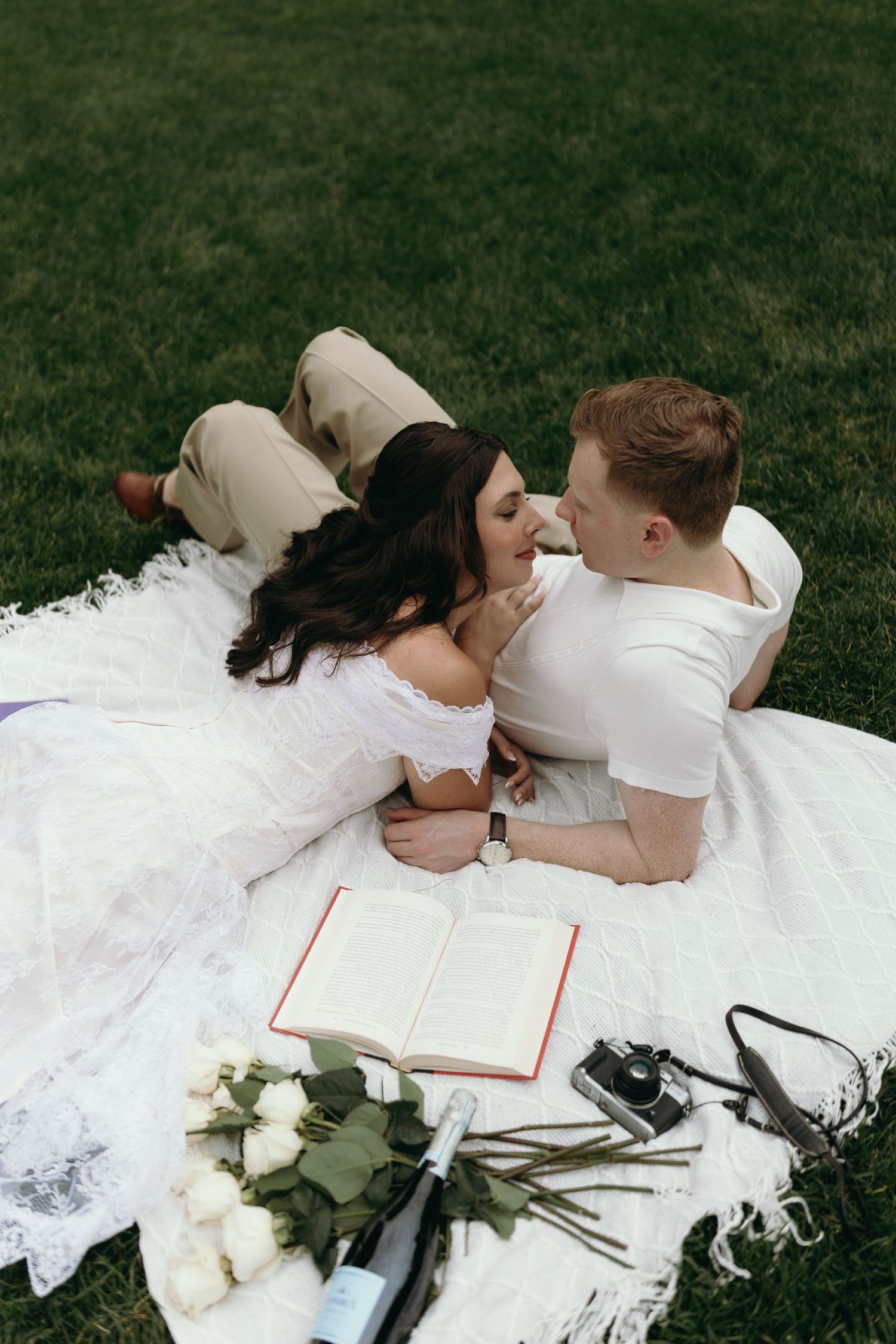 A couple in wedding attire lies on grass reading books together in romantic photoshoot series.